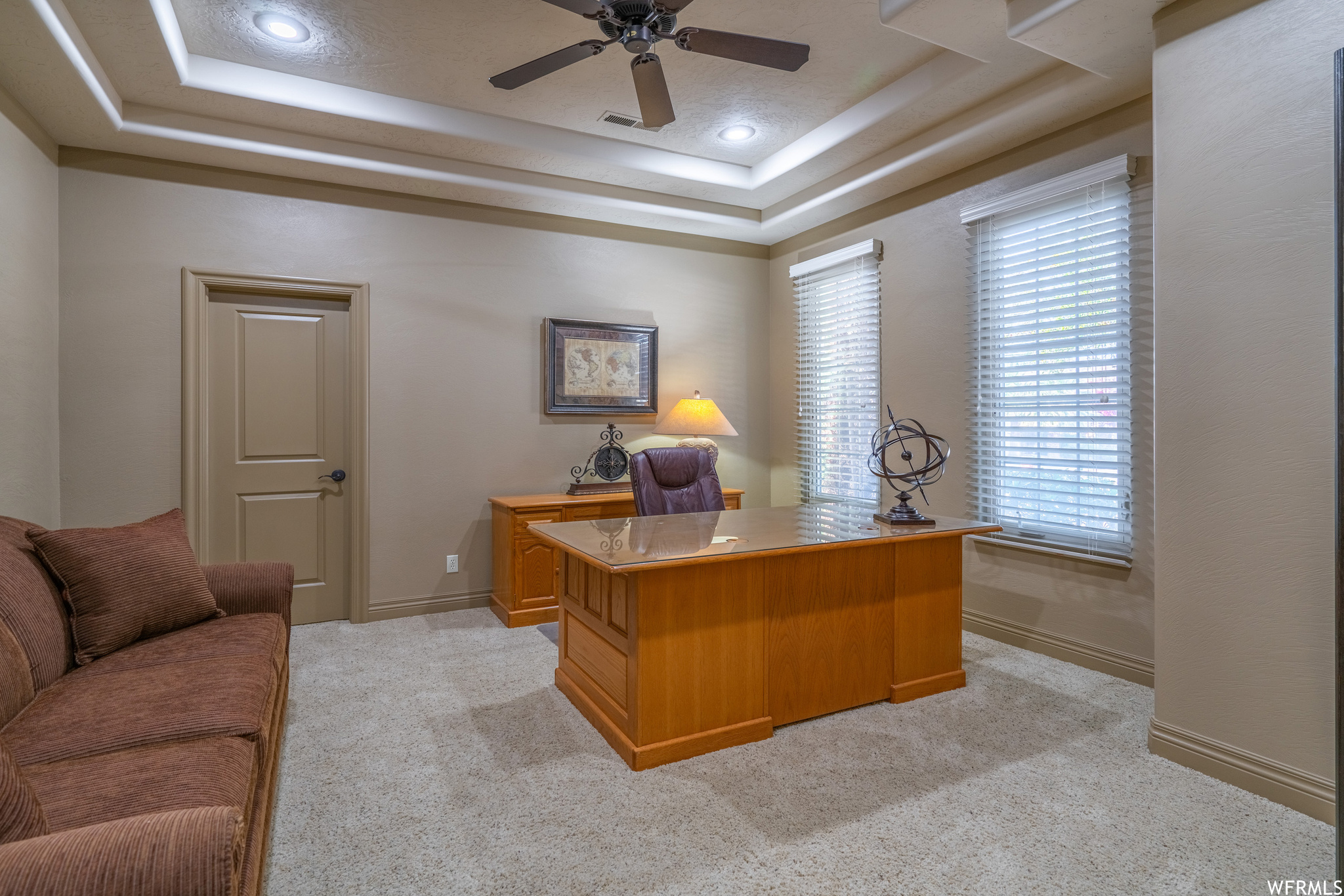 Office space with ceiling fan, a tray ceiling, and light carpet