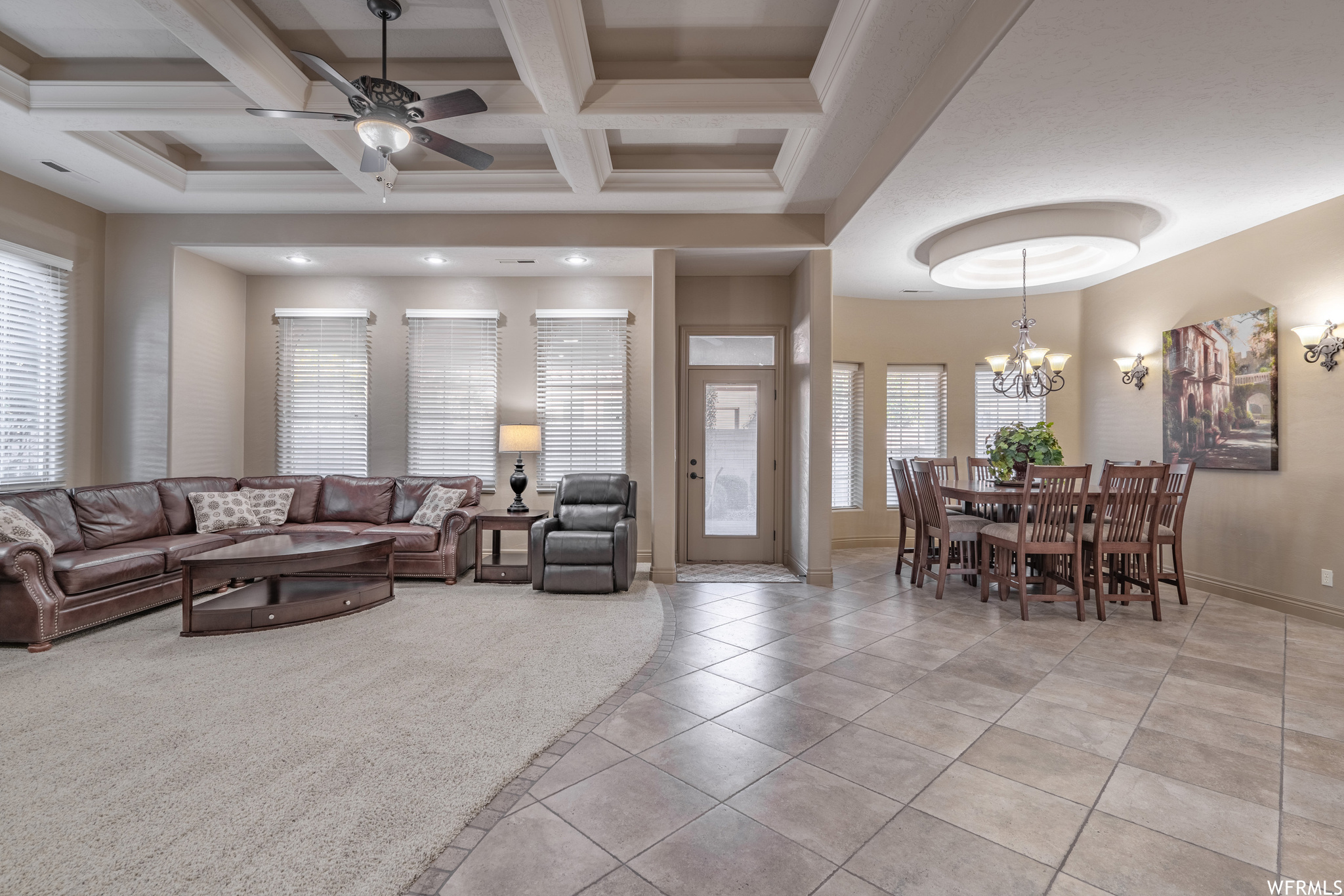 Tiled living room featuring beamed ceiling, a wealth of natural light, coffered ceiling, and ceiling fan with notable chandelier