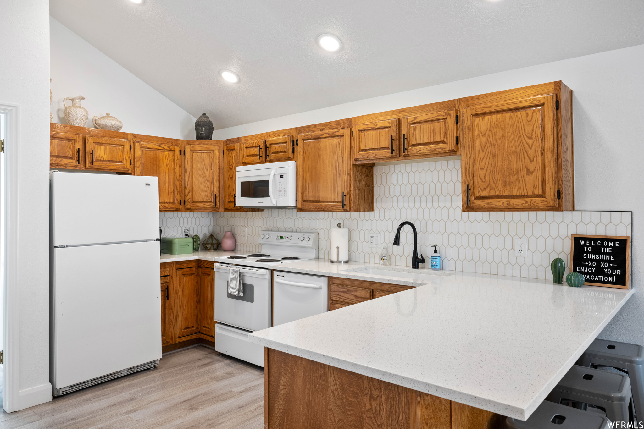 Kitchen featuring lofted ceiling, tasteful backsplash, white appliances, light hardwood / wood-style flooring, and kitchen peninsula