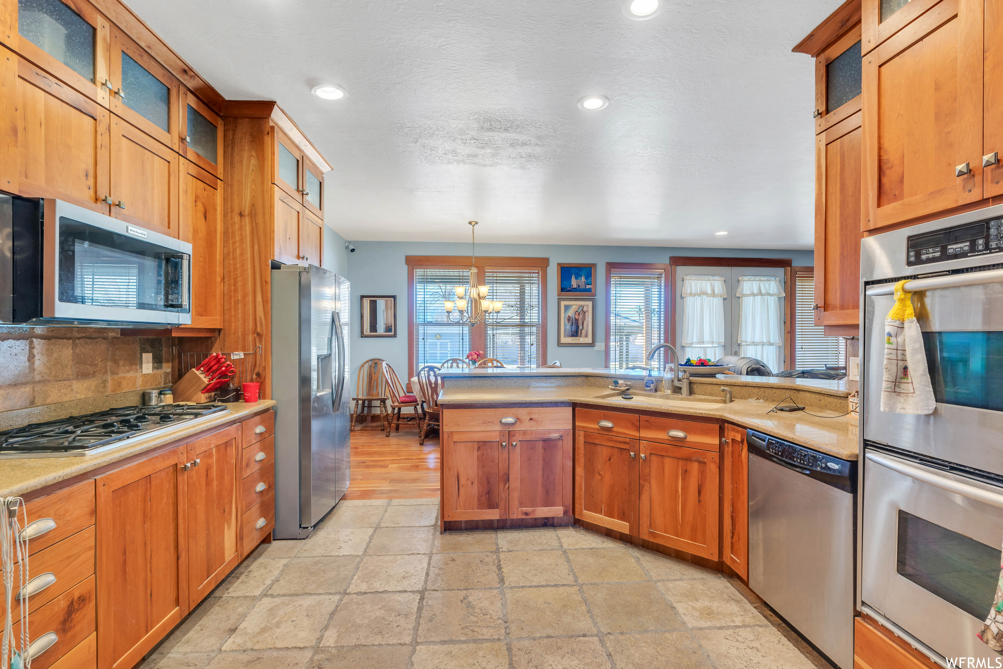 Kitchen with a notable chandelier, sink, stainless steel appliances, decorative light fixtures, and light tile floors