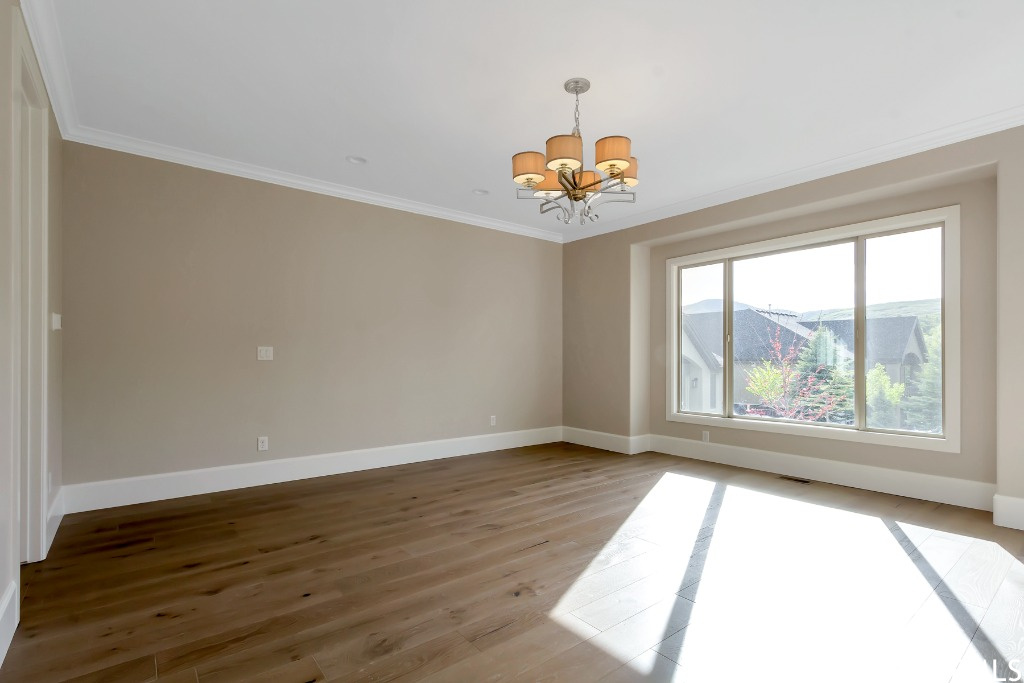 Spare room with a chandelier, crown molding, and light hardwood / wood-style floors