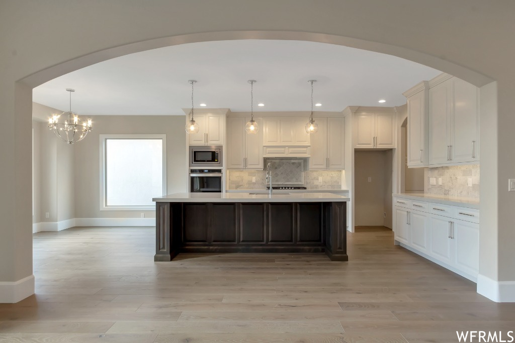 Kitchen with backsplash, an island with sink, a notable chandelier, and appliances with stainless steel finishes