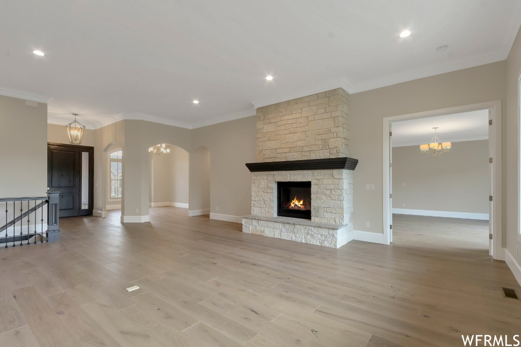 Unfurnished living room featuring crown molding, a stone fireplace, and light hardwood / wood-style flooring