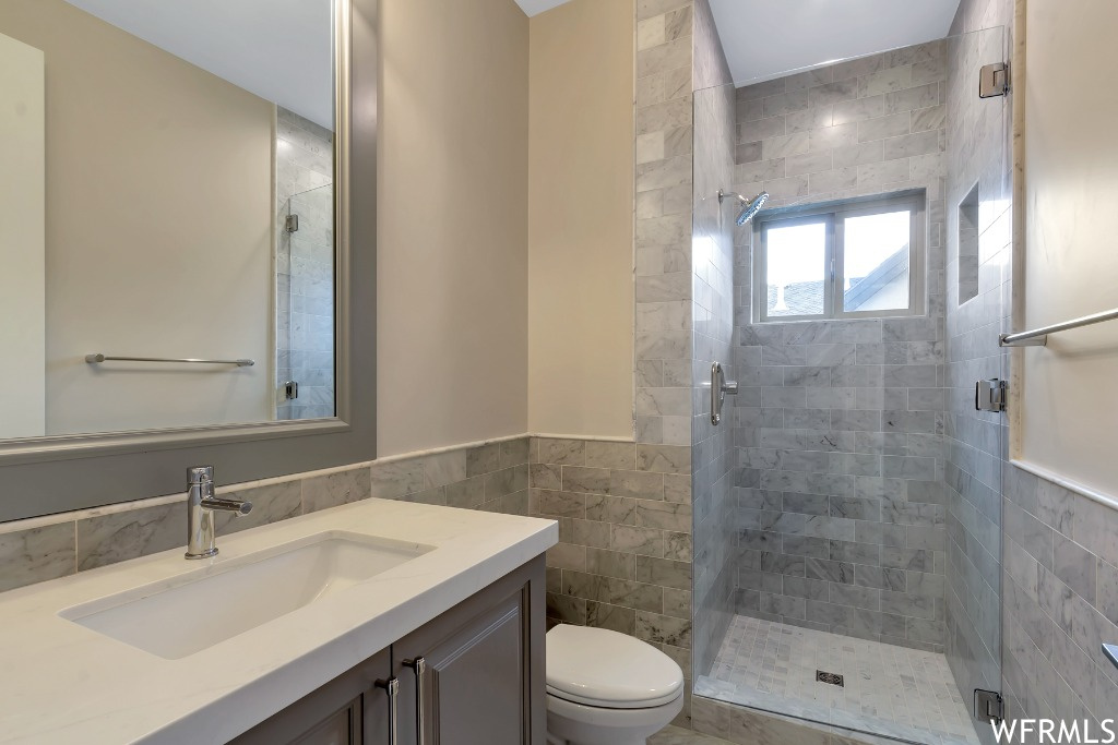 Bathroom featuring toilet, an enclosed shower, tile walls, and vanity with extensive cabinet space