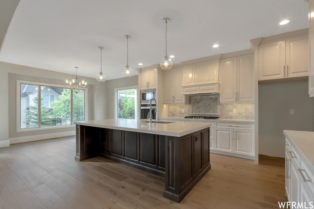 Kitchen featuring a chandelier, a center island with sink, appliances with stainless steel finishes, light wood-type flooring, and tasteful backsplash