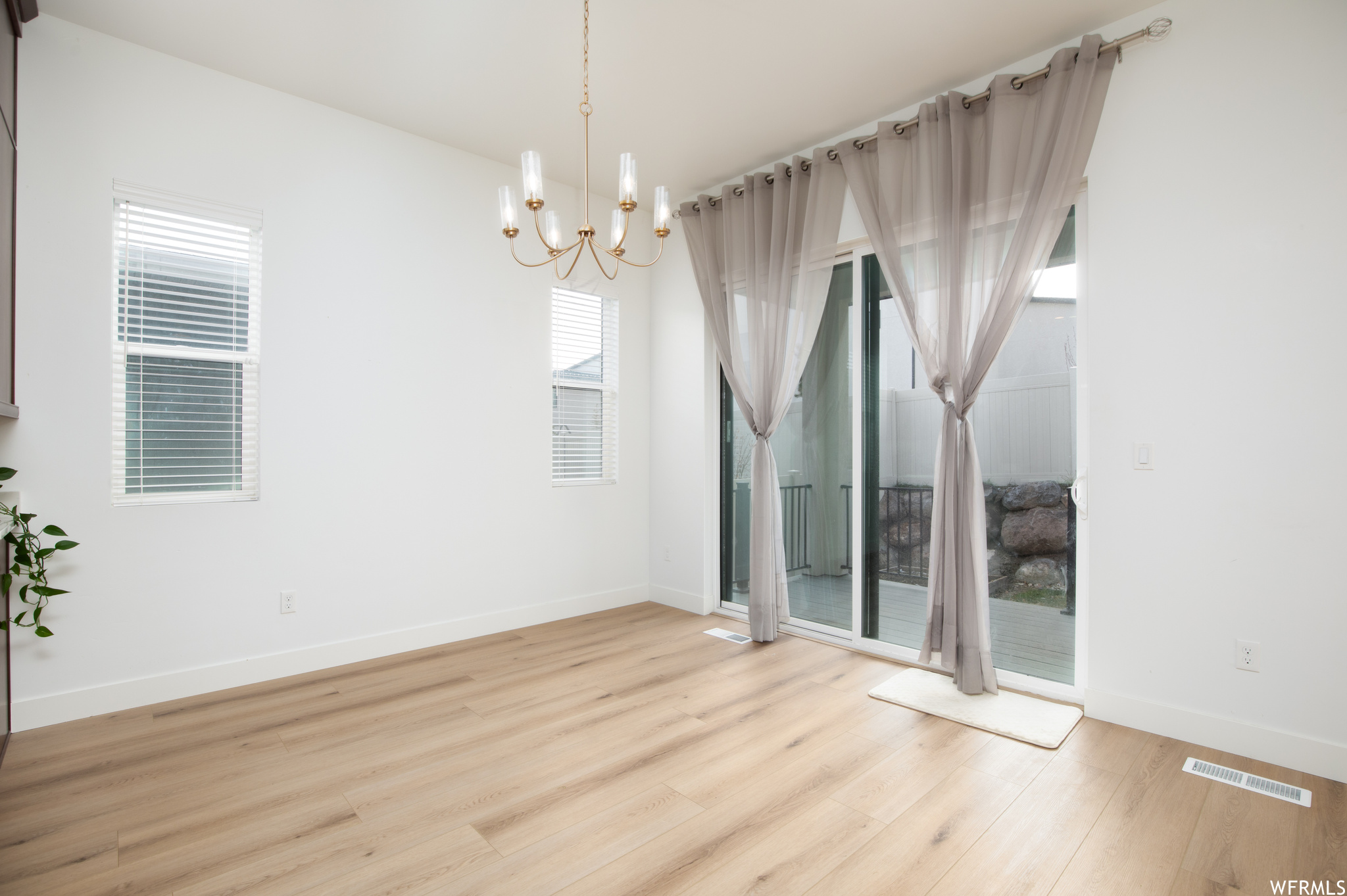 Empty room with light hardwood / wood-style floors and a chandelier