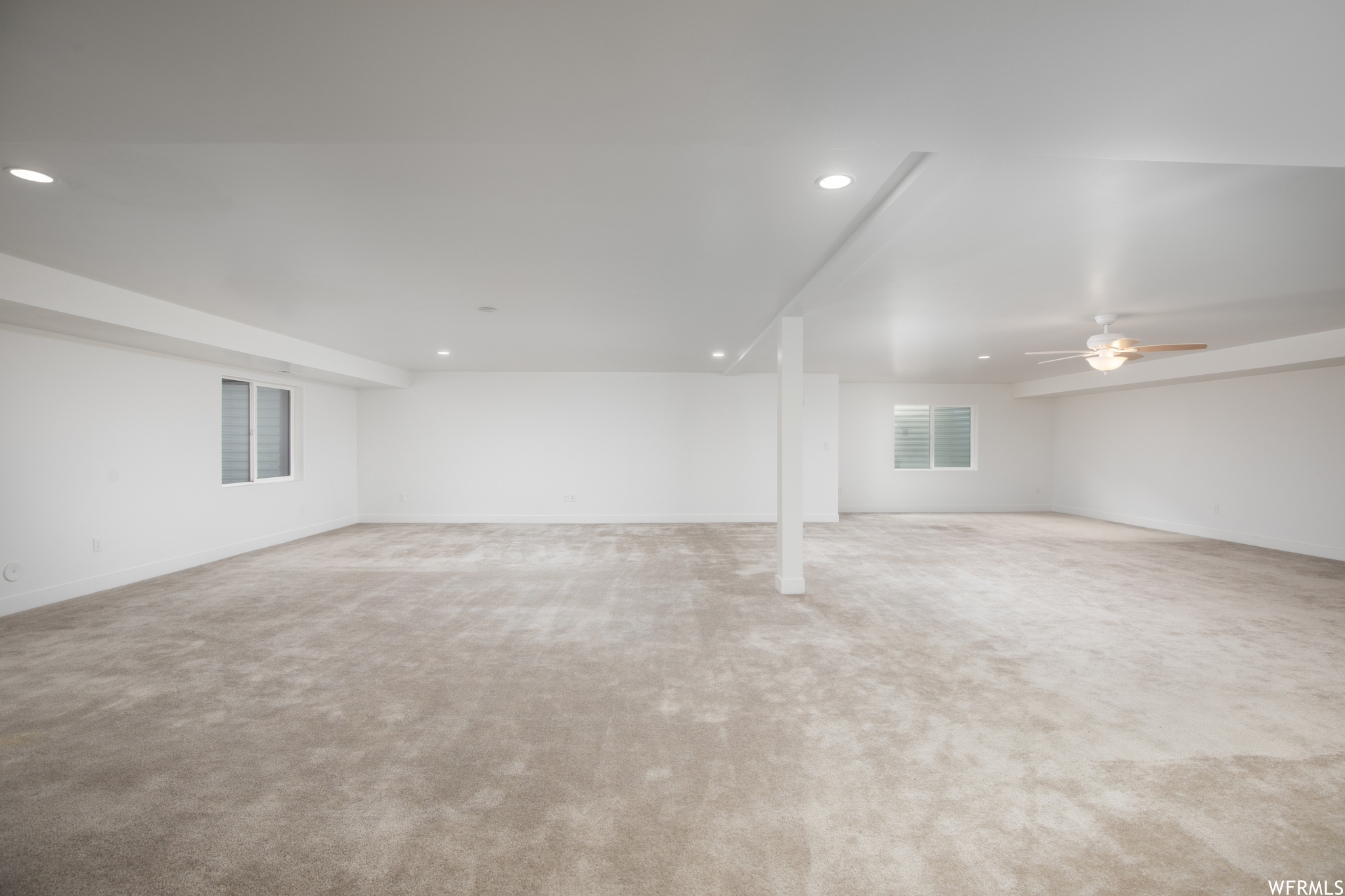 Basement with ceiling fan and light colored carpet