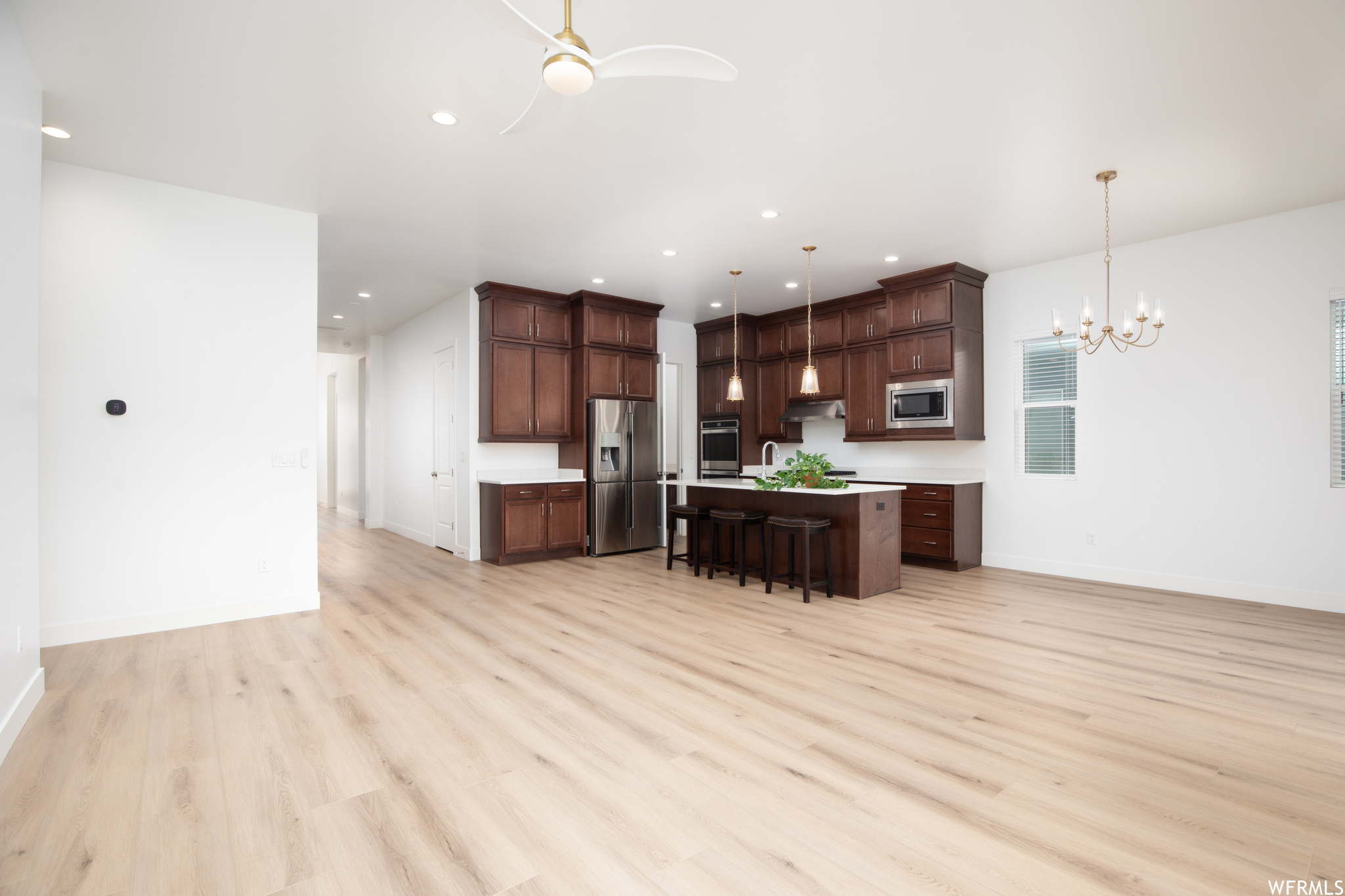 Kitchen with light hardwood / wood-style flooring, a breakfast bar area, hanging light fixtures, and appliances with stainless steel finishes