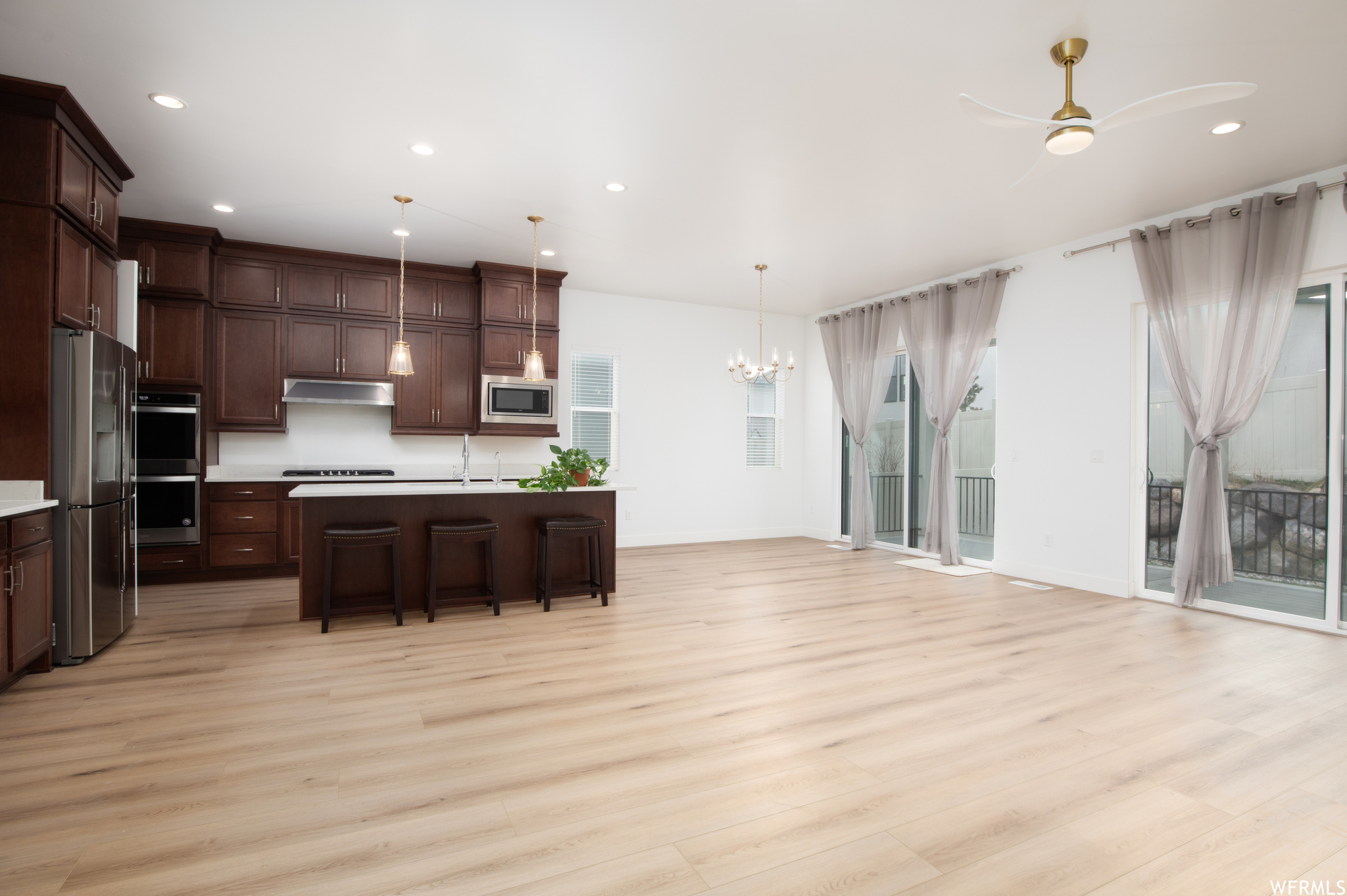 Kitchen featuring light hardwood / wood-style flooring, pendant lighting, ceiling fan with notable chandelier, and appliances with stainless steel finishes