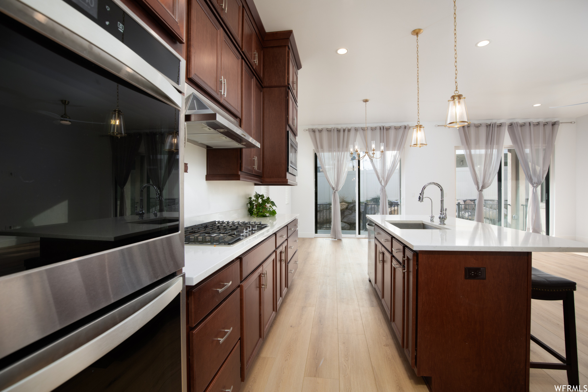 Kitchen featuring hanging light fixtures, sink, appliances with stainless steel finishes, a kitchen island with sink, and light hardwood / wood-style flooring