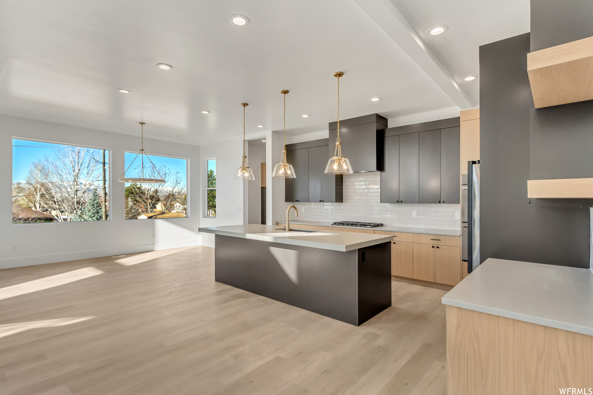 Kitchen featuring sink, light hardwood / wood-style floors, tasteful backsplash, decorative light fixtures, and a center island with sink