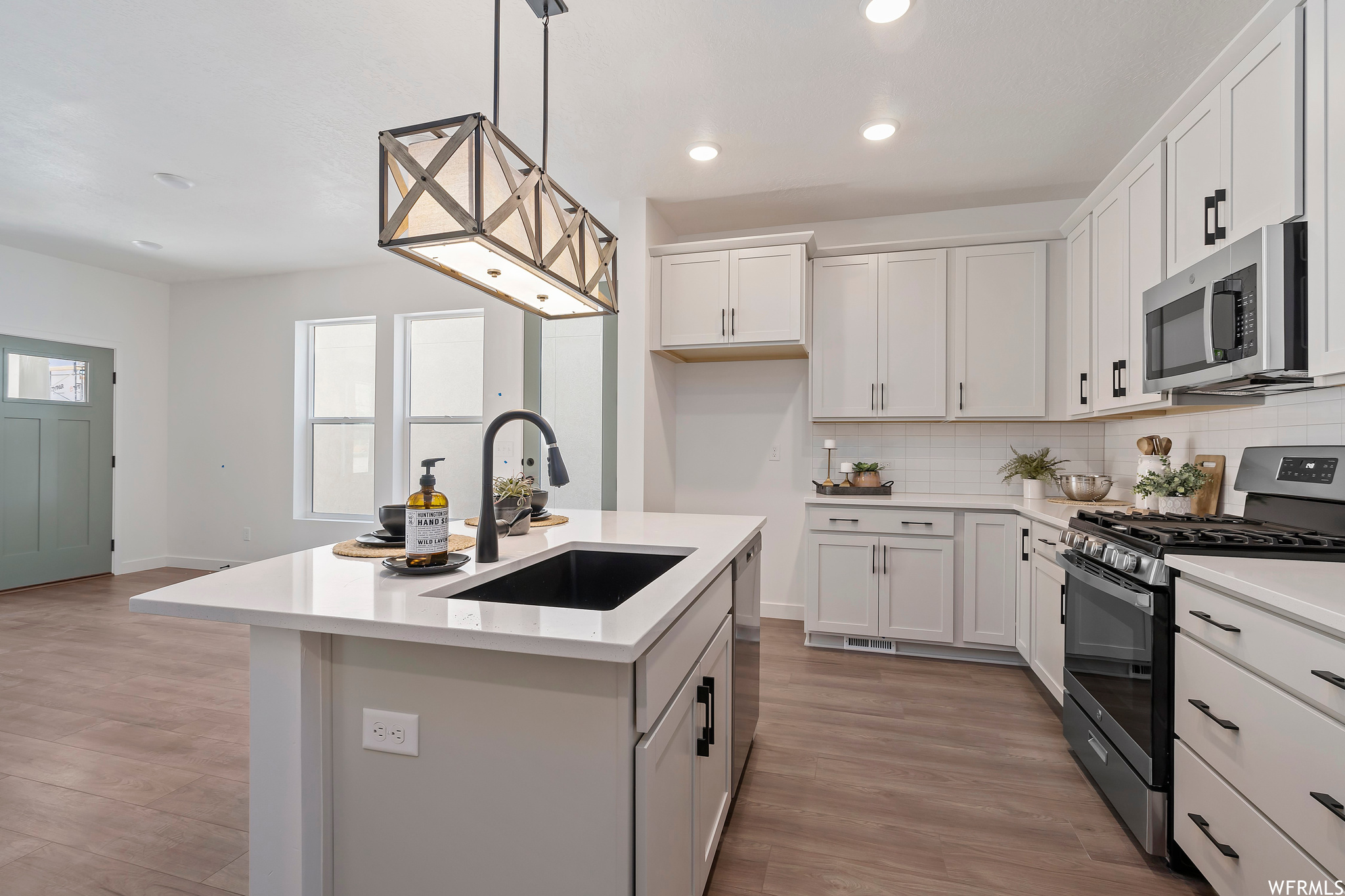 Kitchen with appliances with stainless steel finishes, light hardwood / wood-style flooring, and white cabinetry