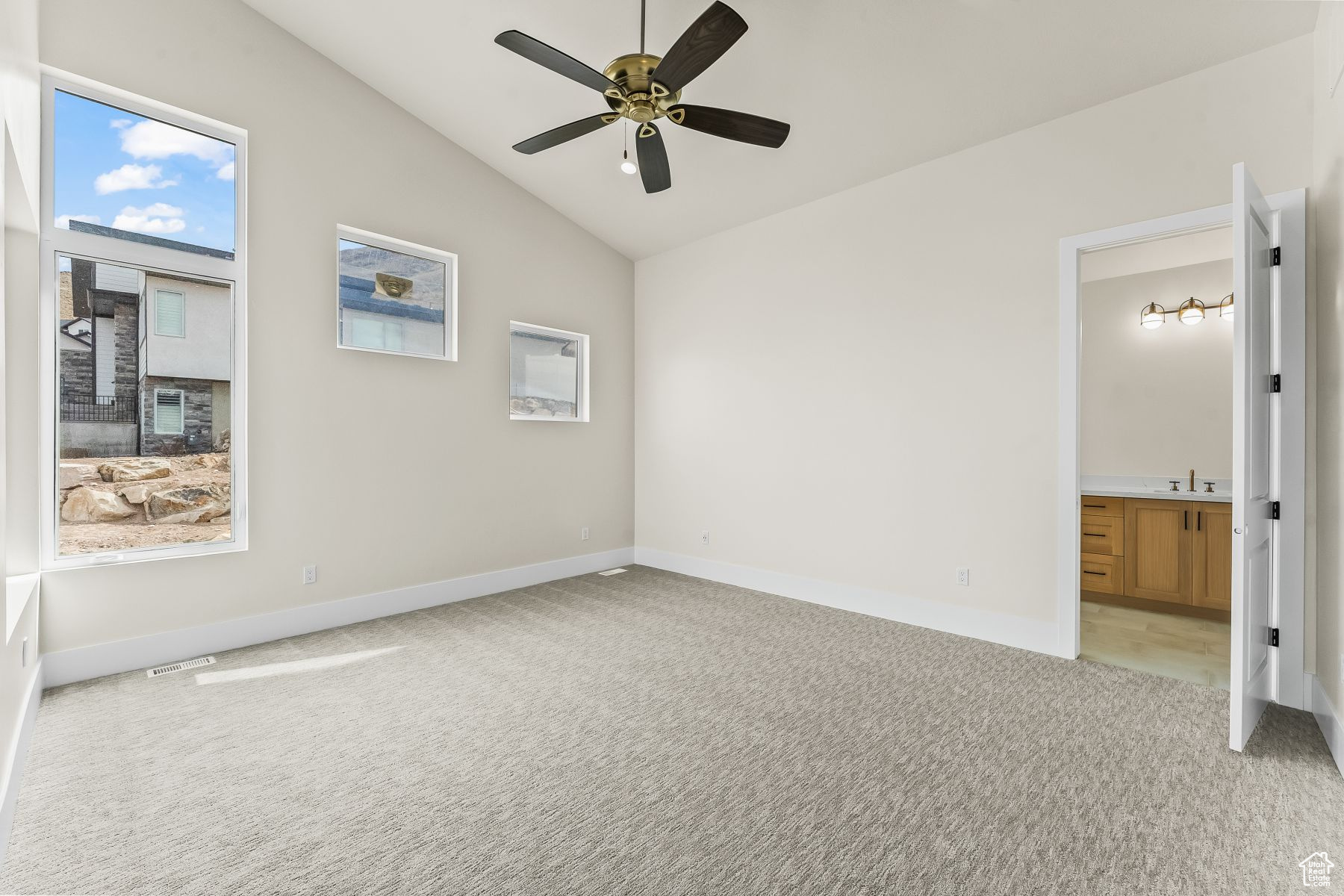 Unfurnished bedroom featuring ceiling fan, light colored carpet, sink, connected bathroom, and lofted ceiling