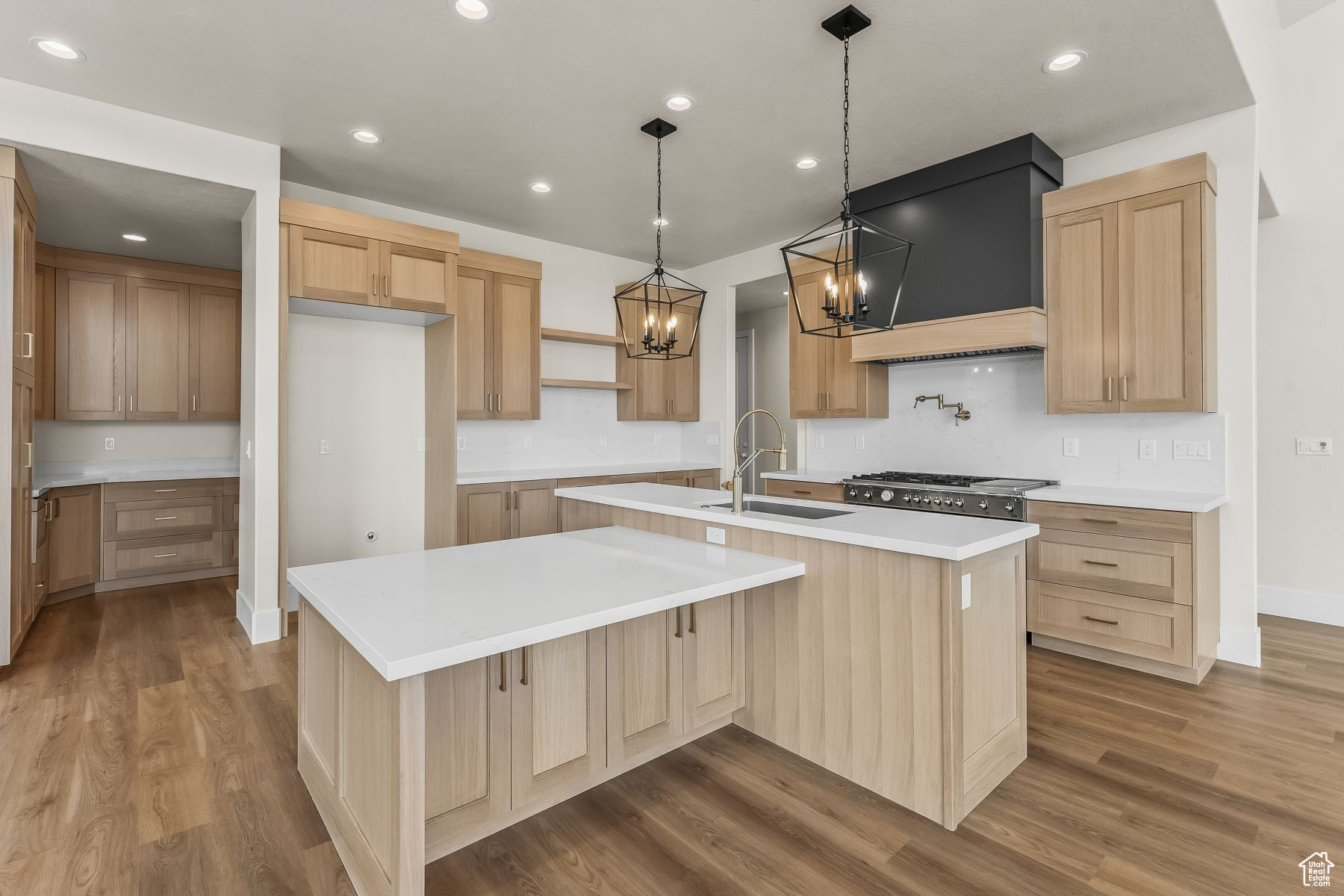 Kitchen with decorative light fixtures, an island with sink, hardwood / wood-style flooring, and premium range hood