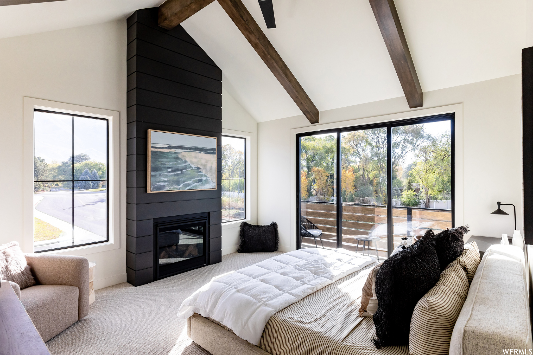 Bedroom featuring multiple windows, light carpet, beam ceiling, and a fireplace