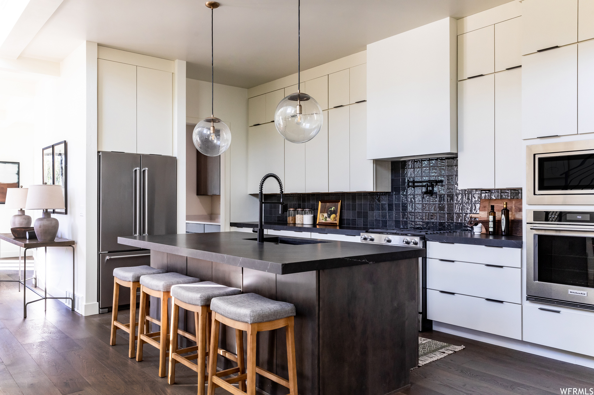 Kitchen with dark hardwood / wood-style flooring, a center island with sink, stainless steel appliances, white cabinets, and backsplash