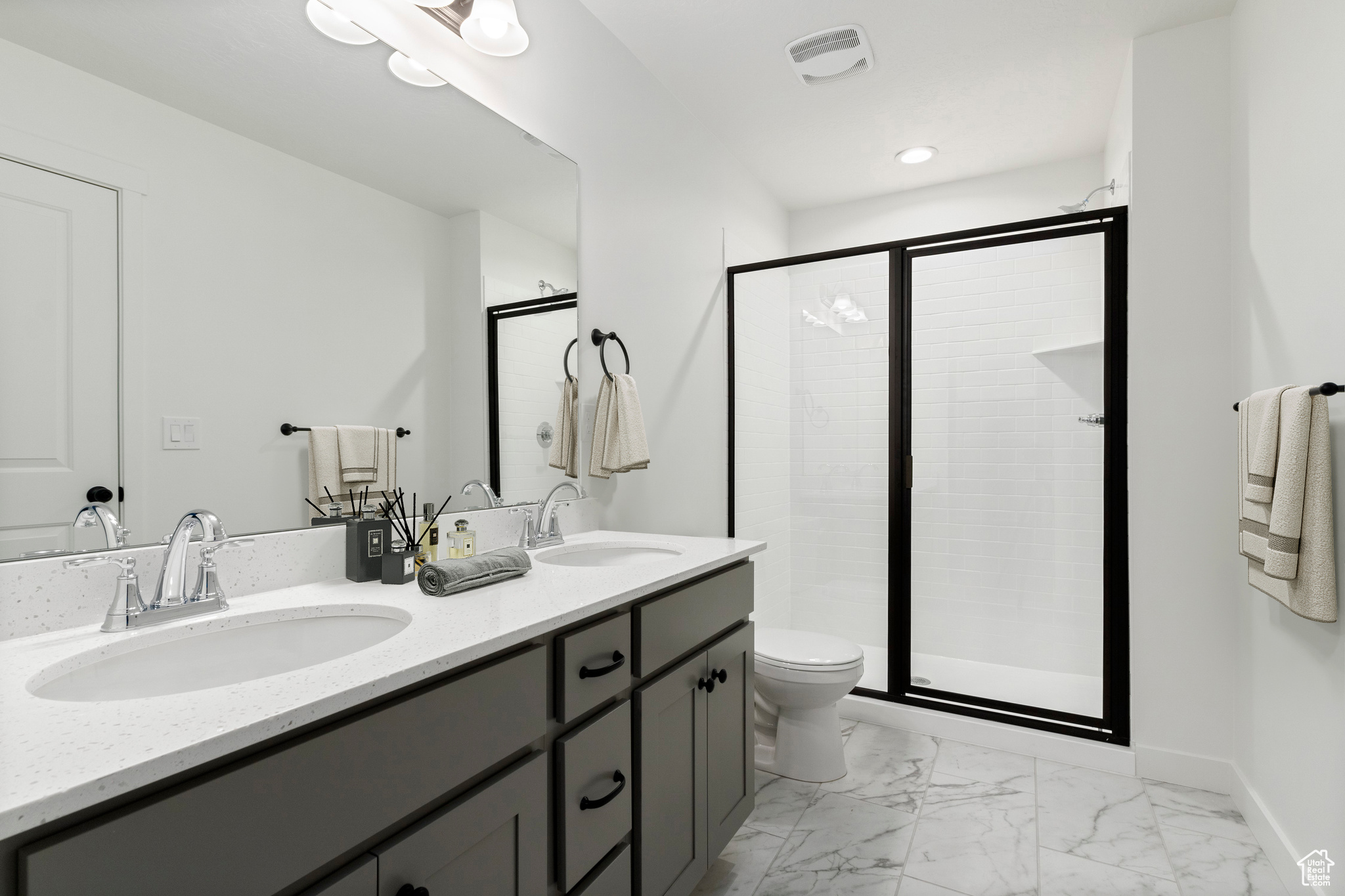 Bathroom with large vanity, double sink, tile floors, a shower with shower door, and toilet
