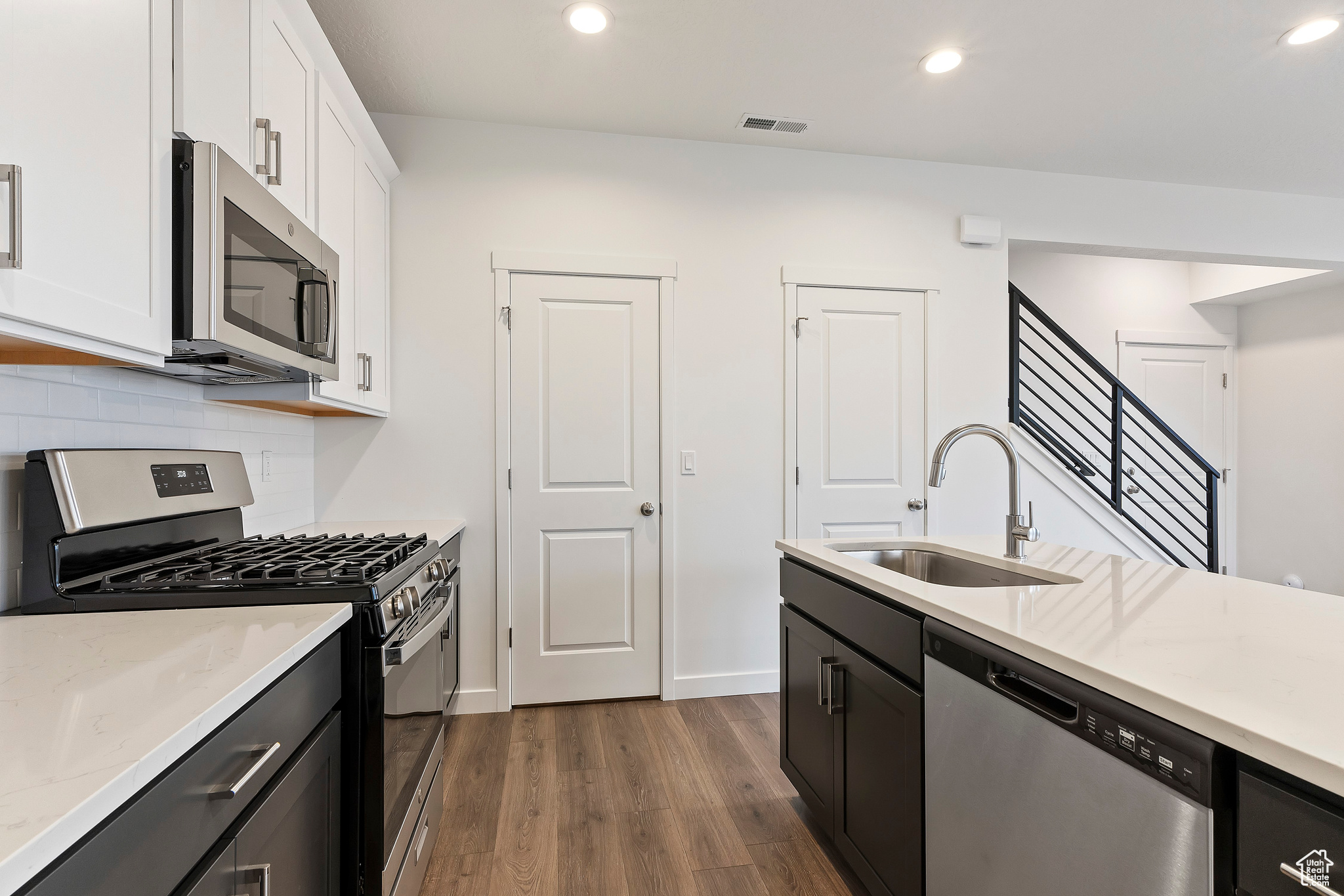 Kitchen featuring decorative backsplash, dark hardwood / wood-style flooring, white cabinetry, sink, and stainless steel appliances