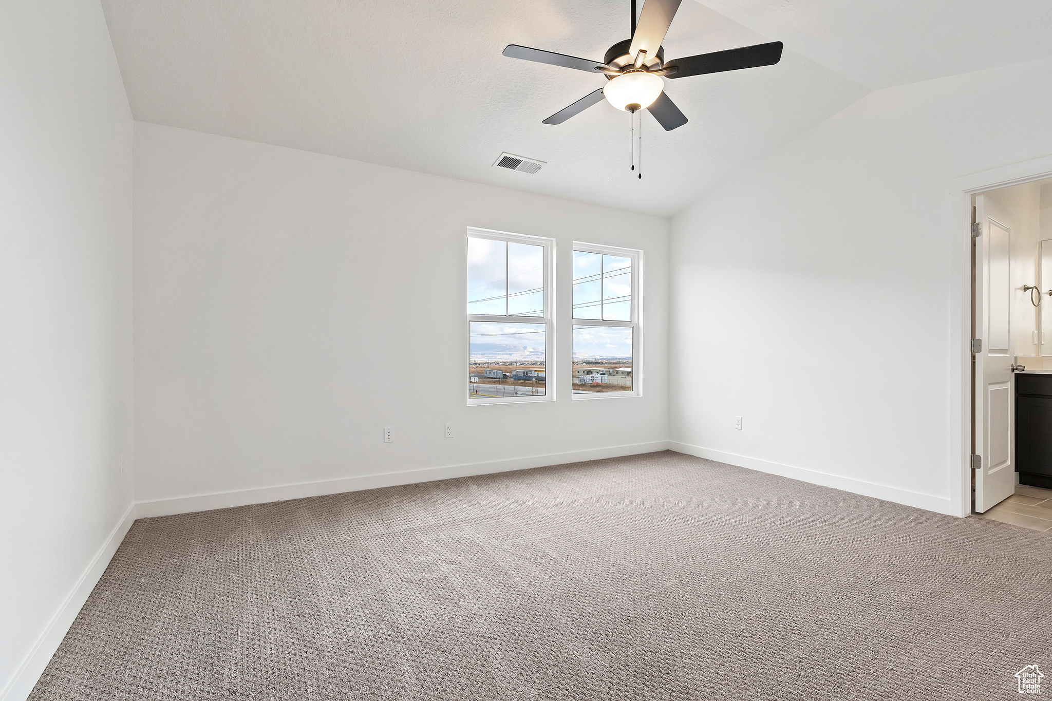 Carpeted empty room featuring ceiling fan and vaulted ceiling