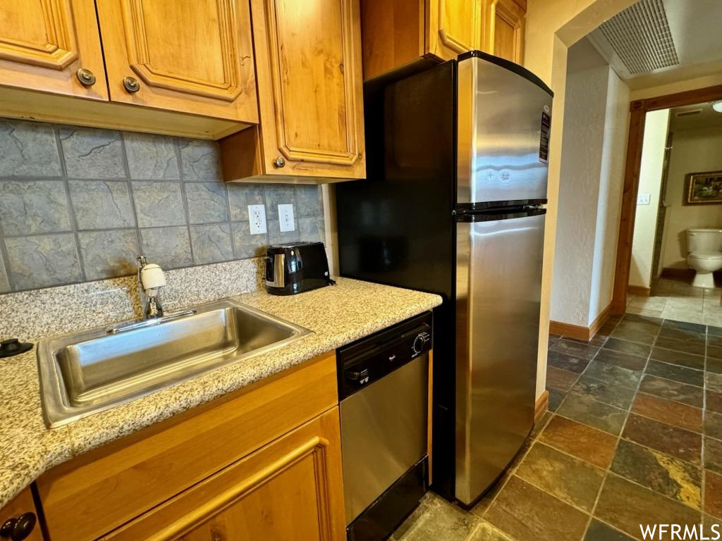 Kitchen with sink, light stone counters, stainless steel dishwasher, dark tile floors, and tasteful backsplash