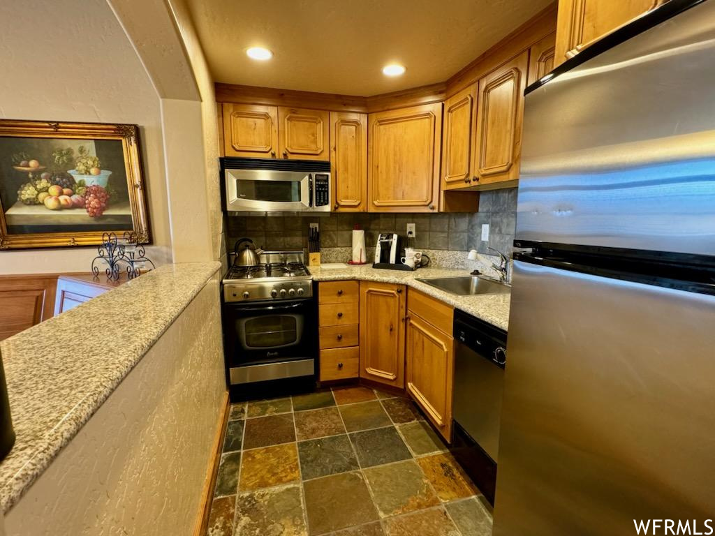 Kitchen featuring dark tile flooring, tasteful backsplash, sink, and appliances with stainless steel finishes