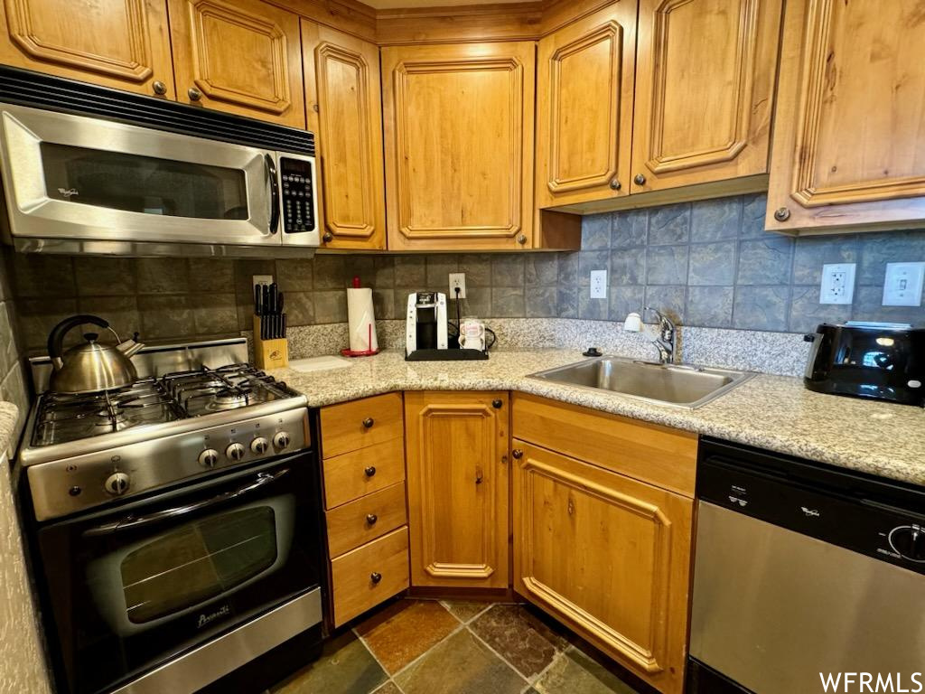 Kitchen with sink, light stone counters, appliances with stainless steel finishes, dark tile flooring, and backsplash