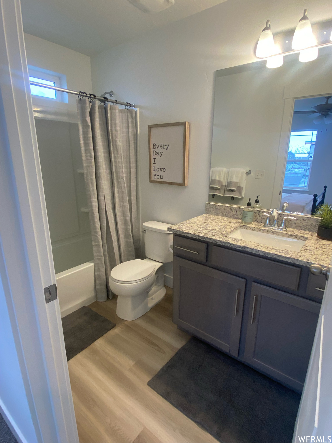 Full bathroom featuring toilet, vanity with extensive cabinet space, ceiling fan, shower / tub combo with curtain, and hardwood / wood-style floors