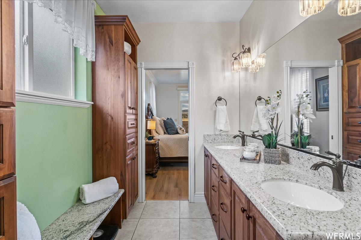 Bathroom with vanity with extensive cabinet space, tile flooring, a wealth of natural light, an inviting chandelier, and double sink