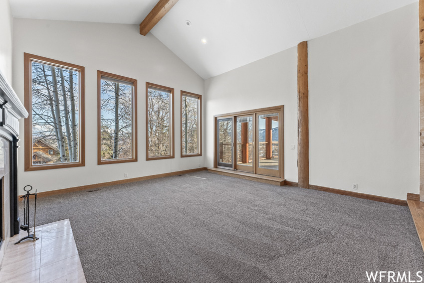 Unfurnished living room featuring light colored carpet, beam ceiling, and high vaulted ceiling
