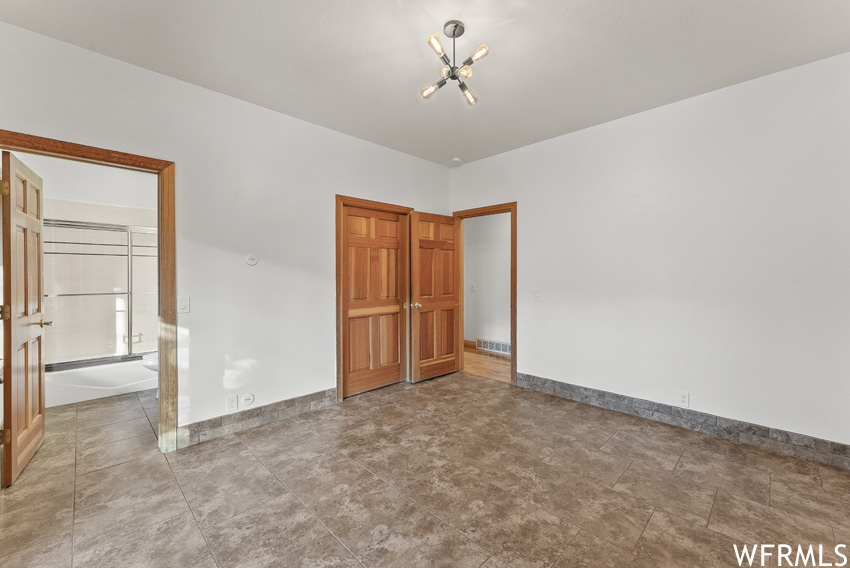 Unfurnished bedroom featuring light tile floors and a notable chandelier