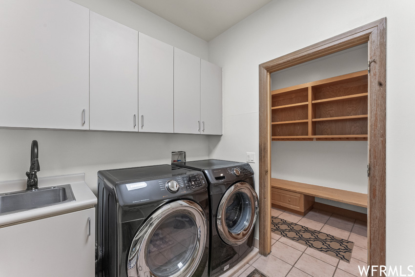 Laundry room featuring light tile floors, sink, washer hookup, cabinets, and washing machine and clothes dryer