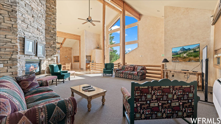 Carpeted living room featuring ceiling fan, a fireplace, beam ceiling, and high vaulted ceiling