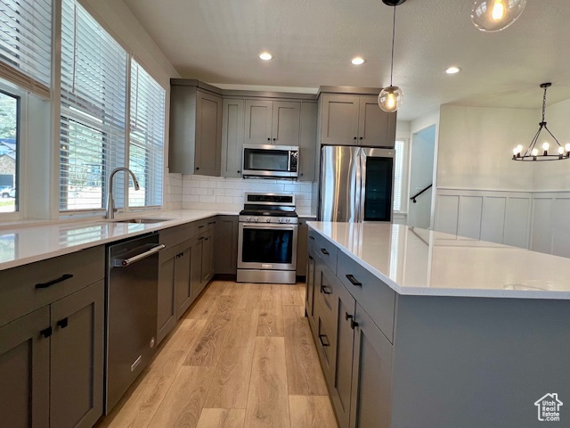 Kitchen featuring hanging light fixtures, light hardwood / wood-style flooring, stainless steel appliances, sink, and tasteful backsplash