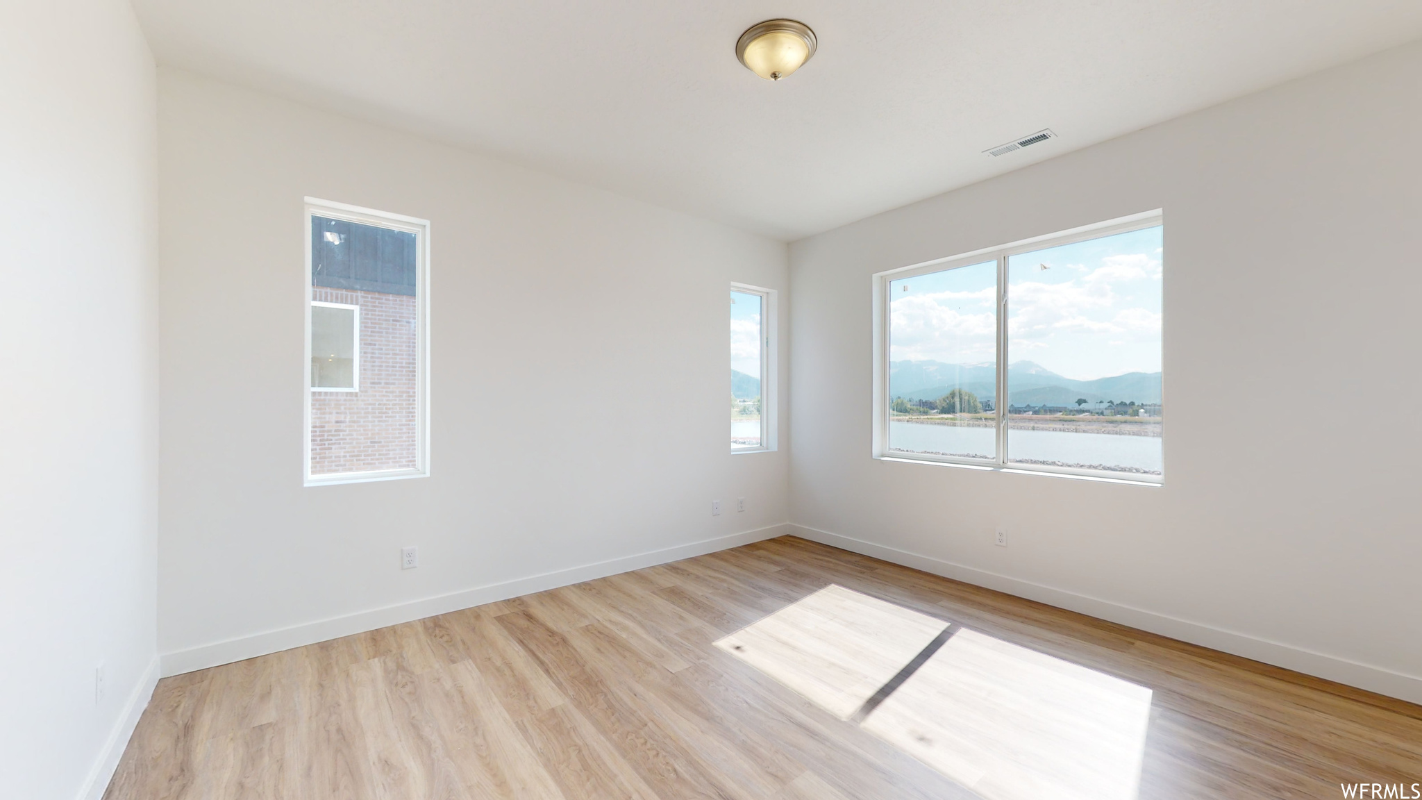 Unfurnished room with light hardwood / wood-style flooring and a water and mountain view