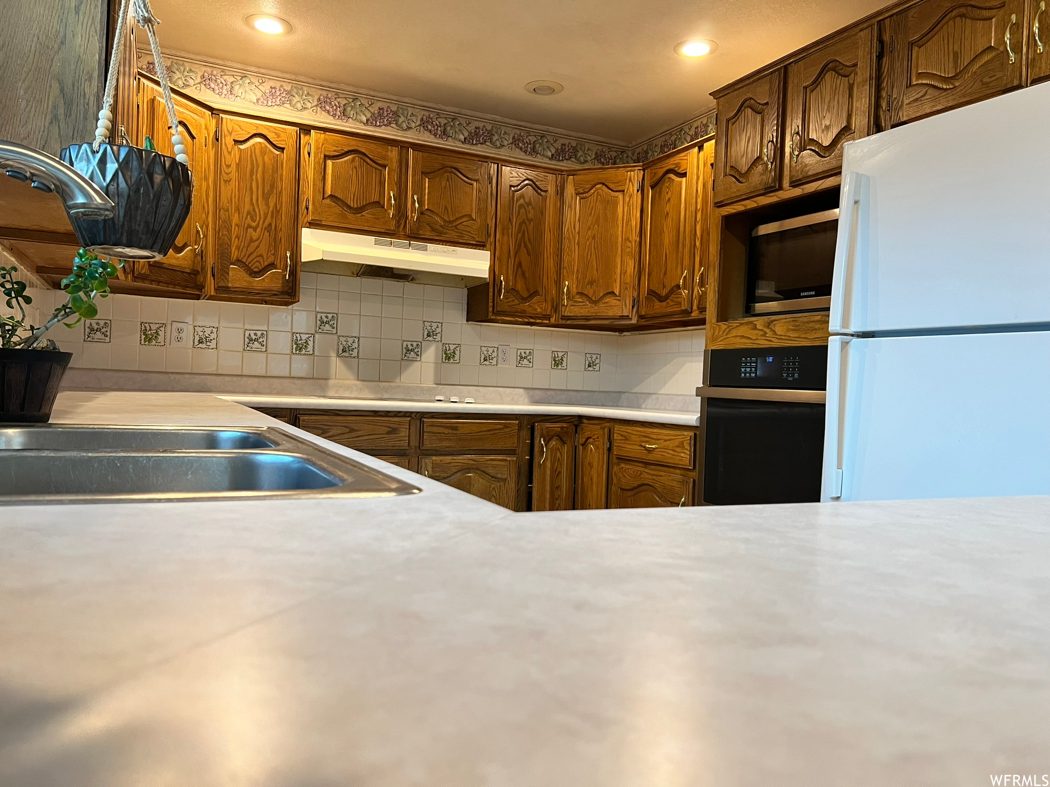 Kitchen with white refrigerator, stainless steel microwave, black oven, and tasteful backsplash