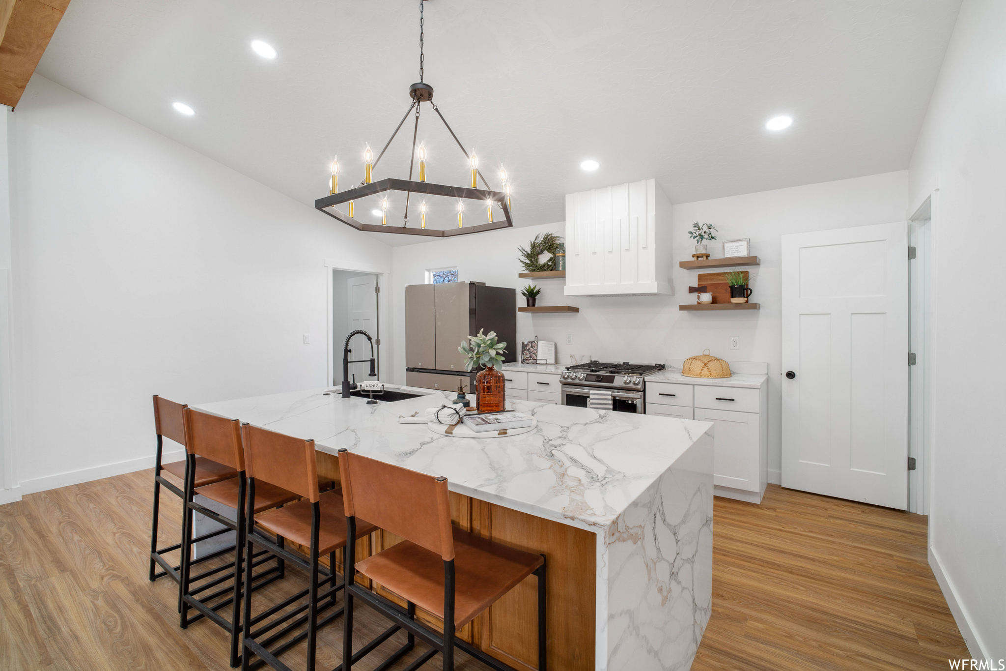 Kitchen with light wood-type flooring, a kitchen island with sink, white cabinets, and stainless steel appliances