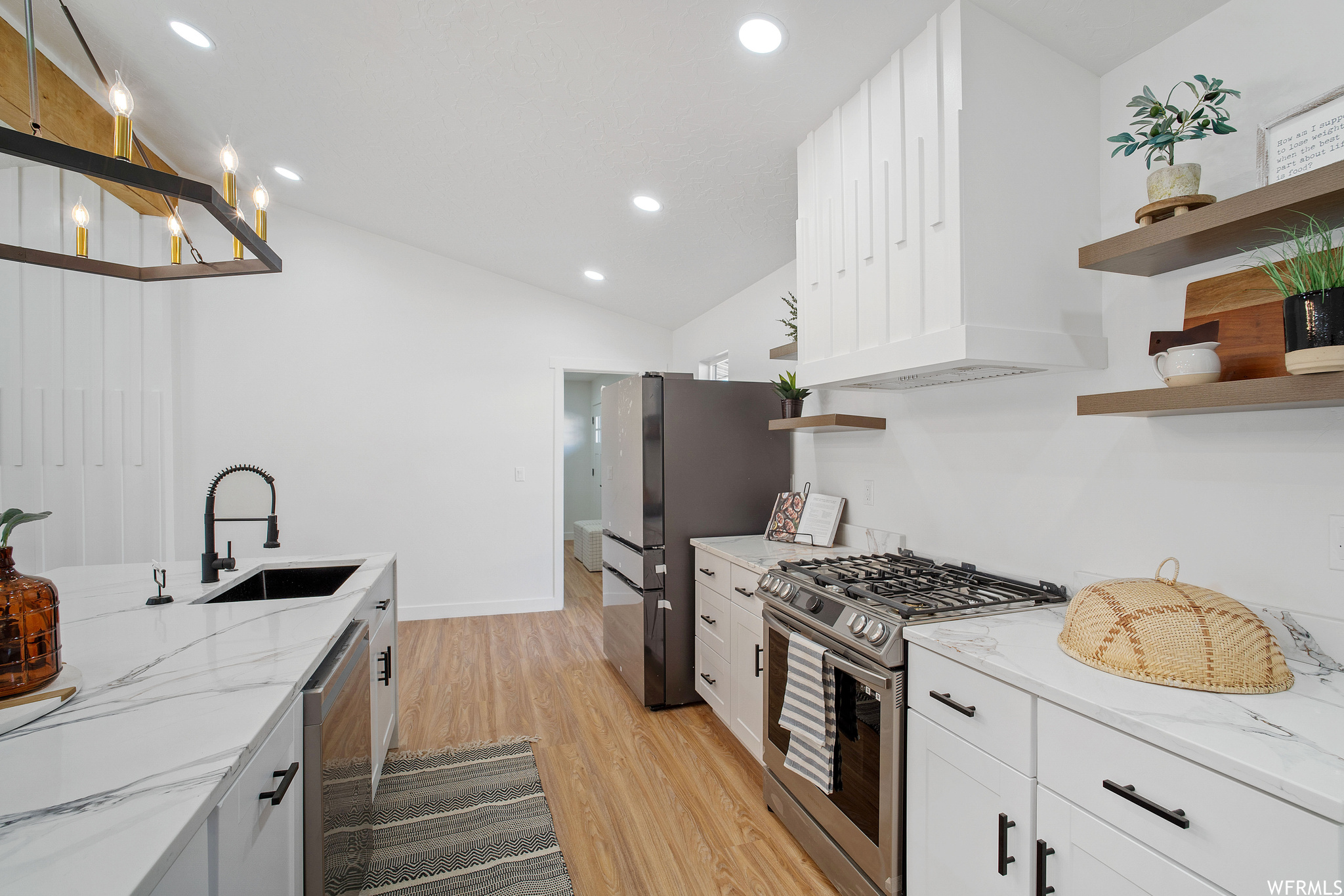 Kitchen featuring white cabinets, sink, lofted ceiling, and stainless steel appliances. Custom hood to compliment the living rooms custom accent wall.