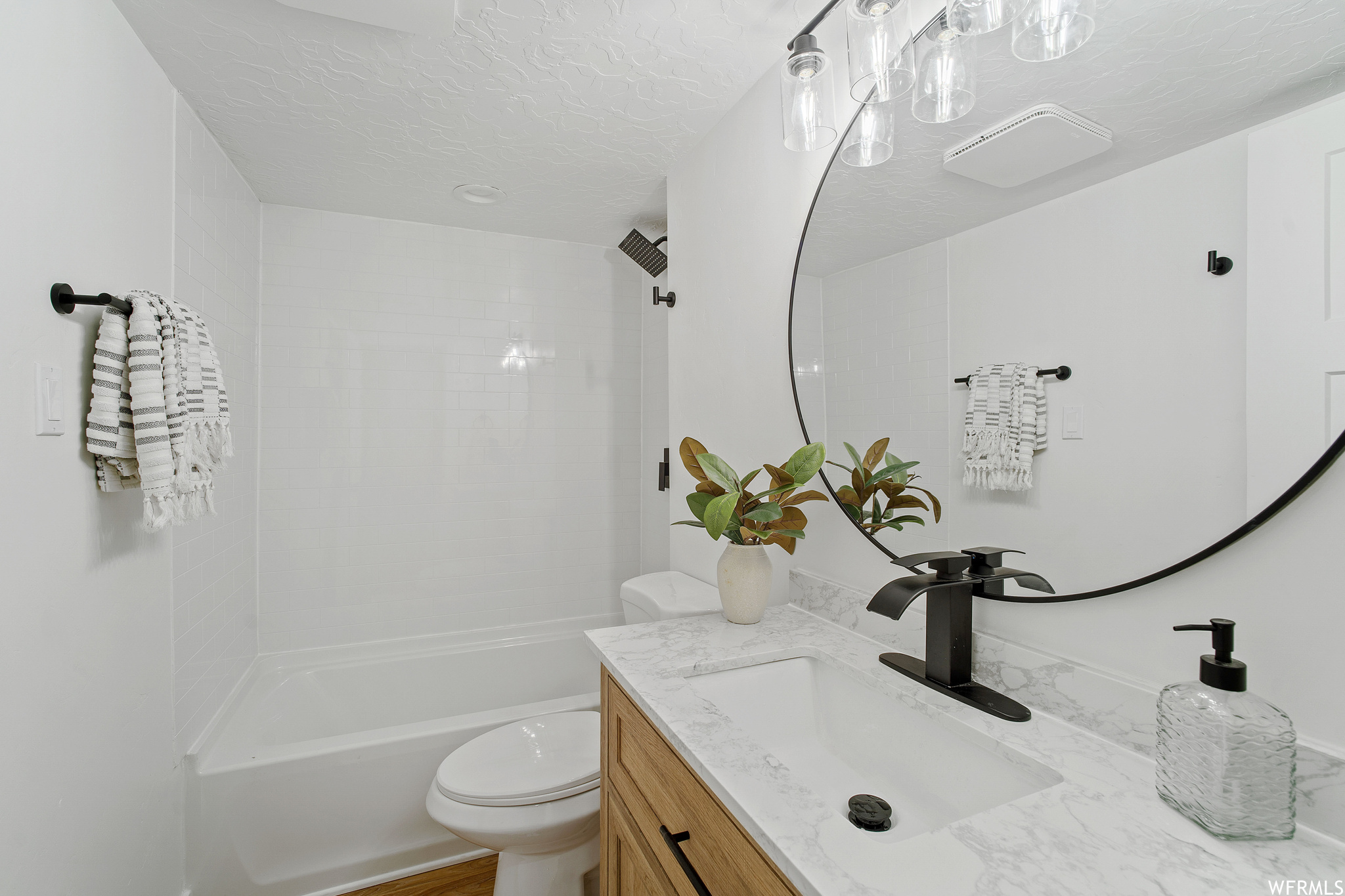Full bathroom with tiled shower / bath, vanity, toilet, and a textured ceiling