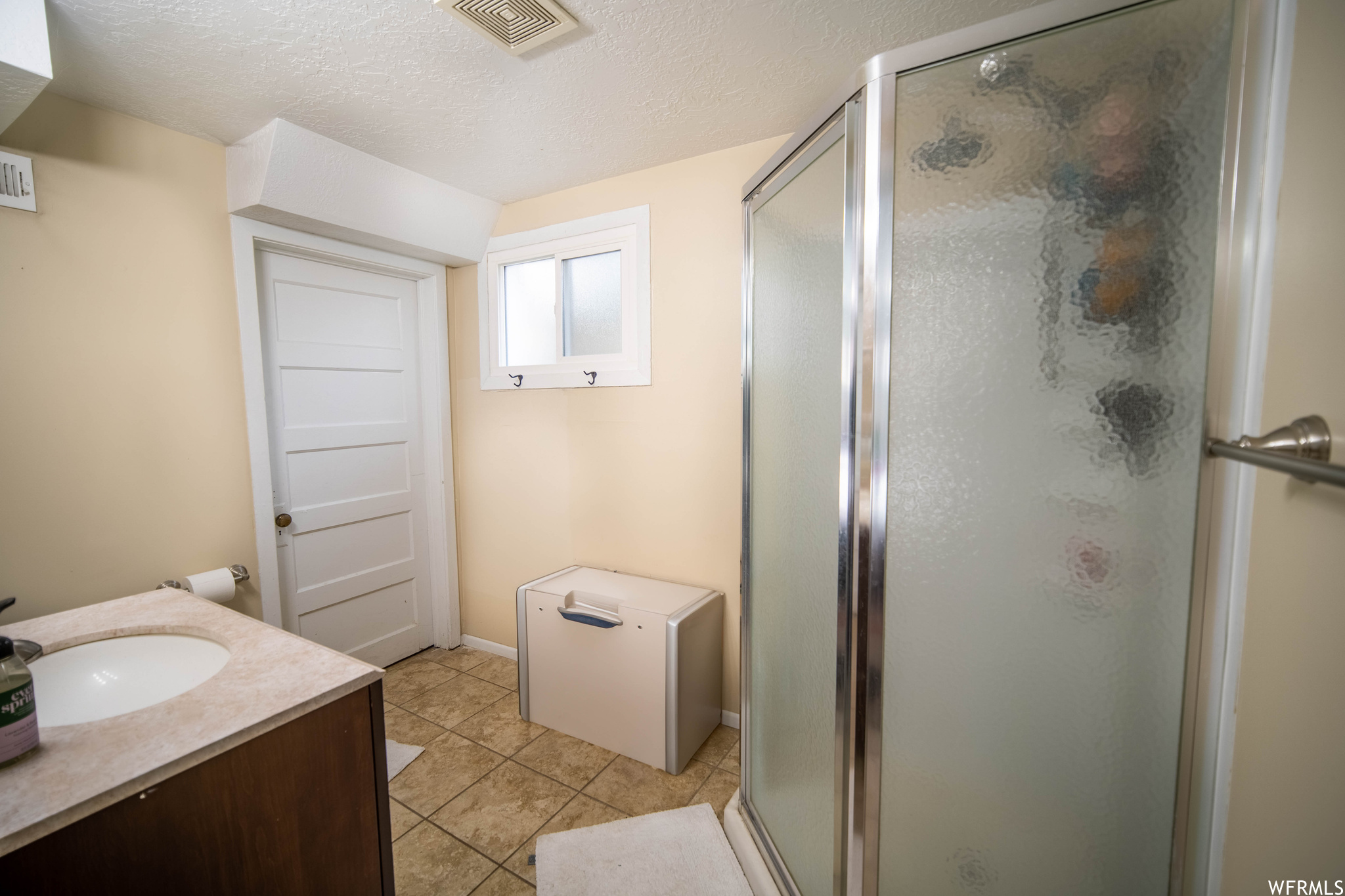 Bathroom with a textured ceiling, vanity, a shower with door, and tile floors
