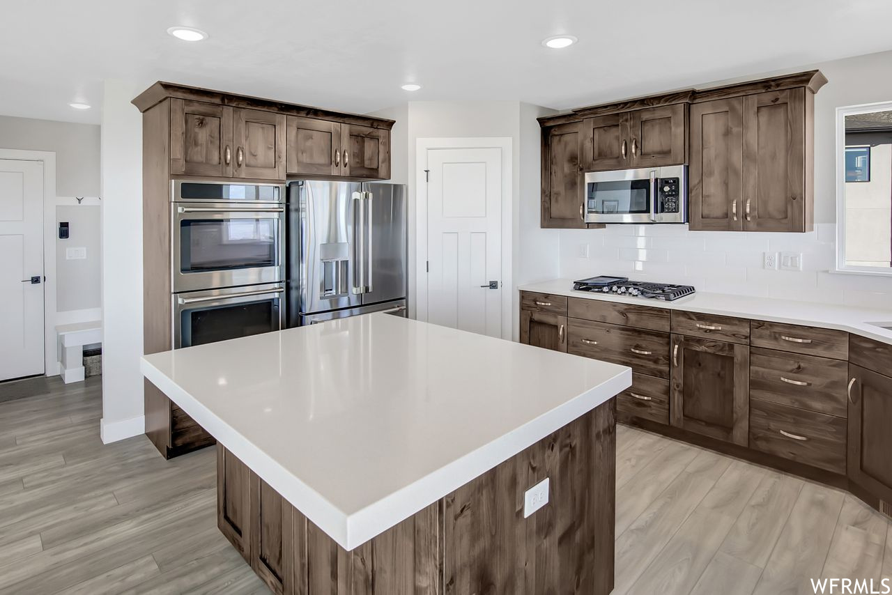 Kitchen featuring stainless steel appliances, light hardwood / wood-style floors, a center island, and backsplash