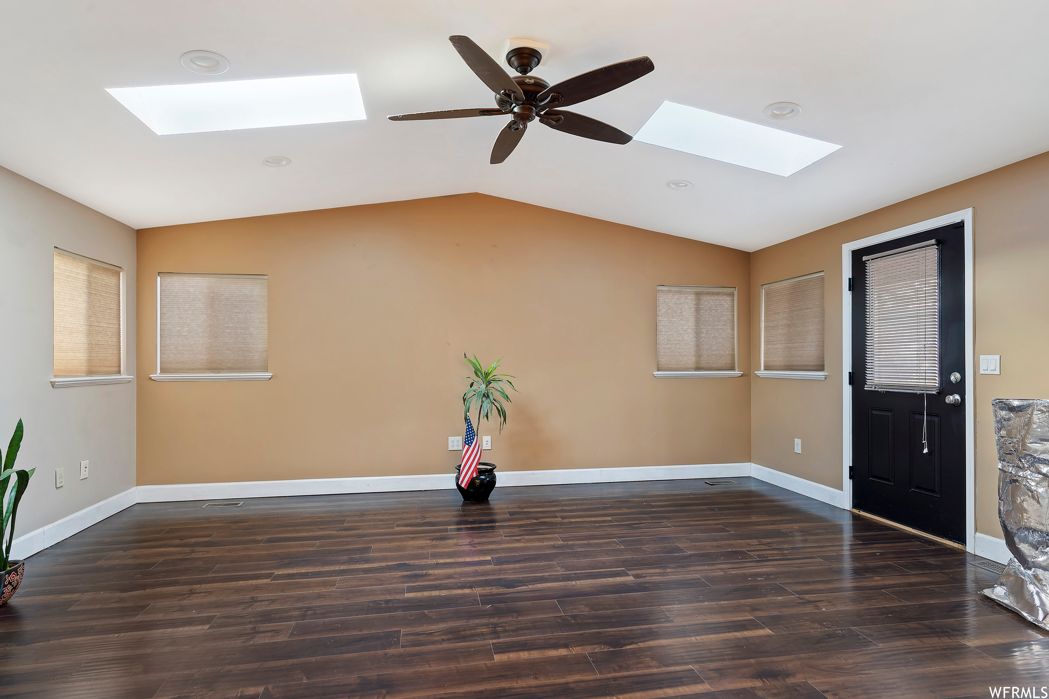 Spare room featuring dark wood-type flooring, ceiling fan, and vaulted ceiling with skylight