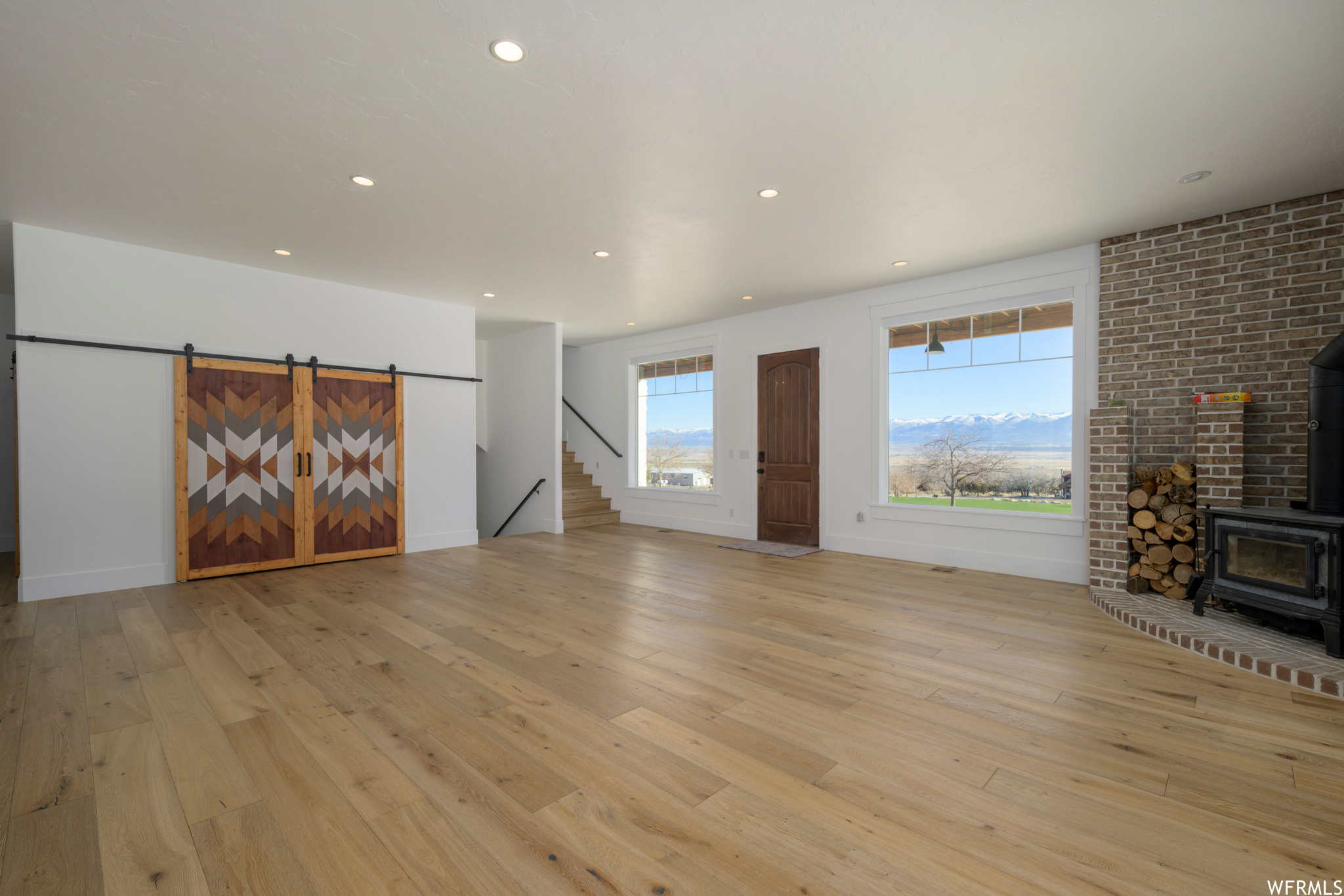 Unfurnished living room with light wood-type flooring, a wood stove, and a barn door