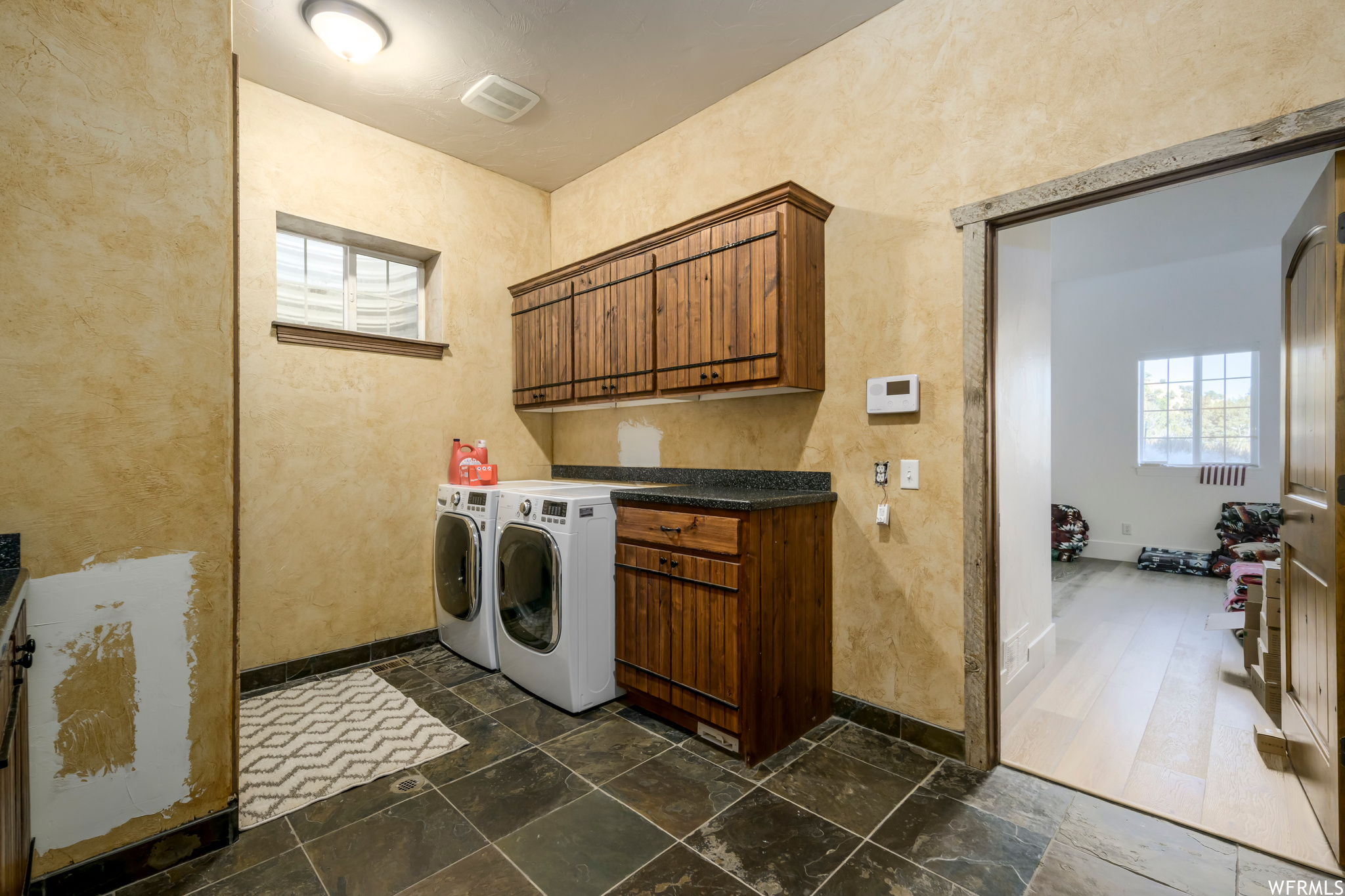 Laundry room featuring dark tile floors, independent washer and dryer, and cabinets