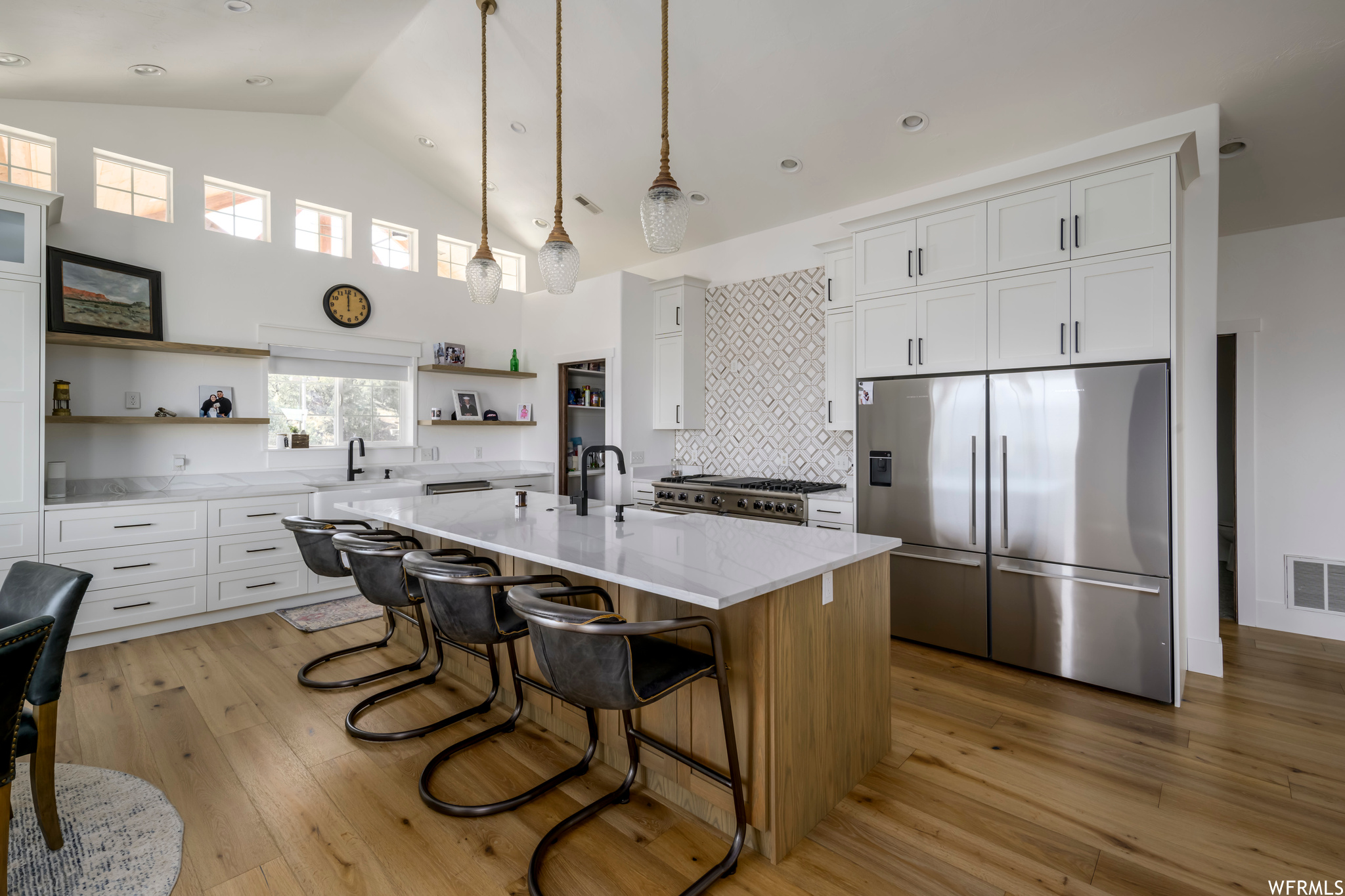 Kitchen with light wood-type flooring, a kitchen island with sink, white cabinetry, and appliances with stainless steel finishes