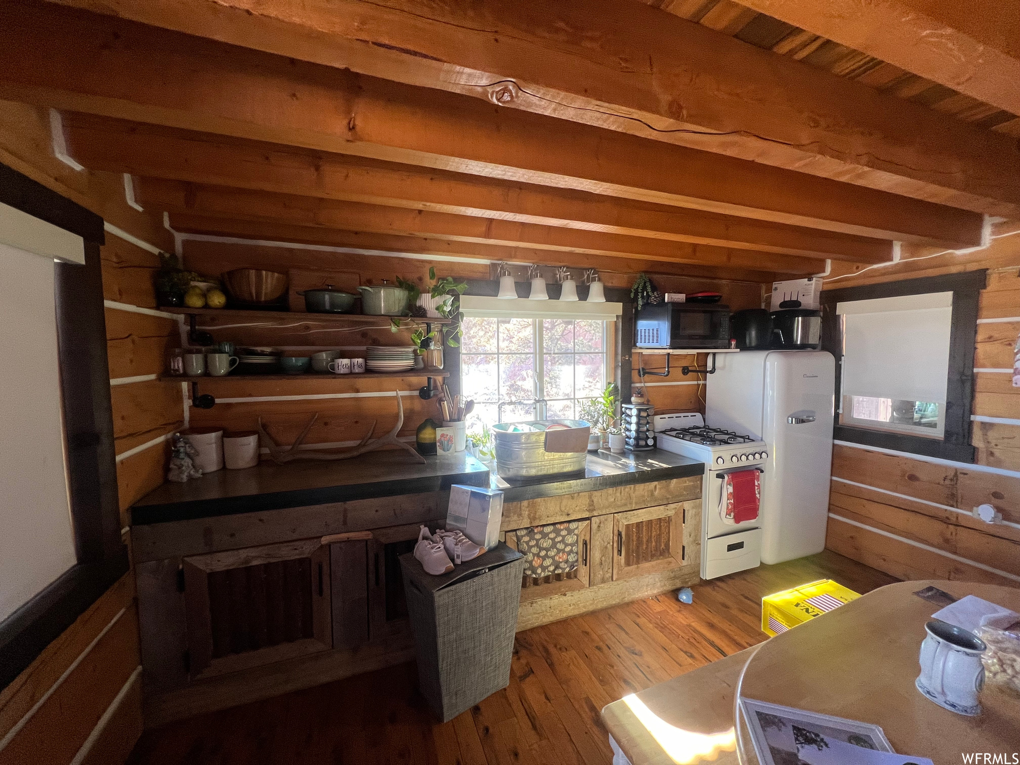Bunk House. Kitchen with white appliances, wooden walls, light hardwood / wood-style flooring, and beam ceiling