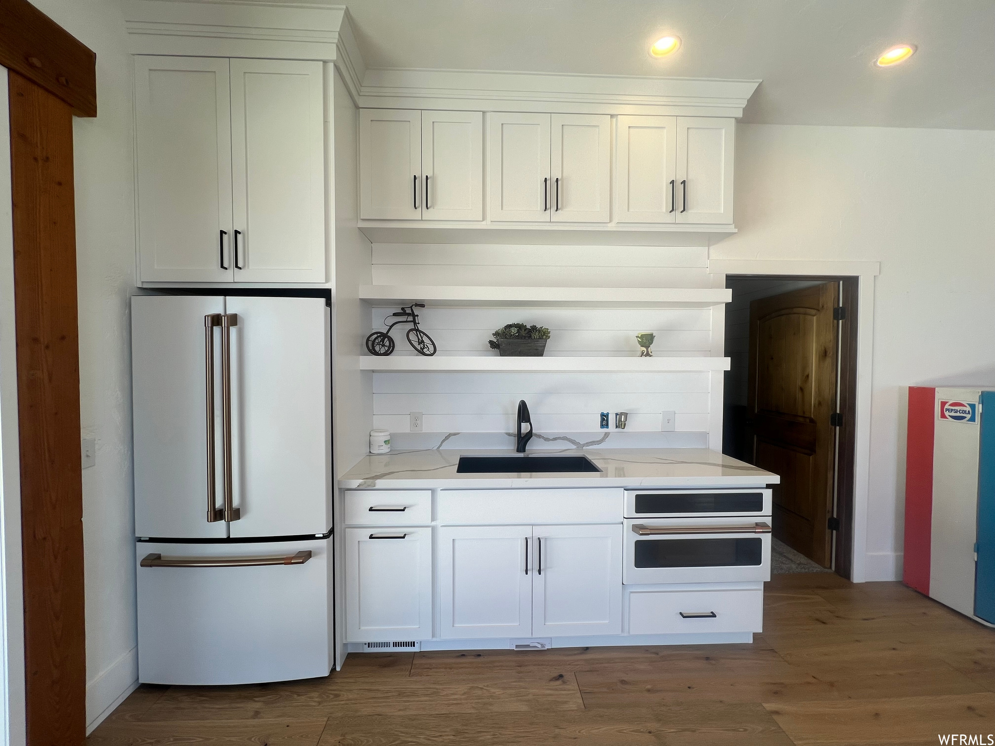 Kitchen featuring sink, high end fridge, hardwood / wood-style floors, oven, and white cabinetry