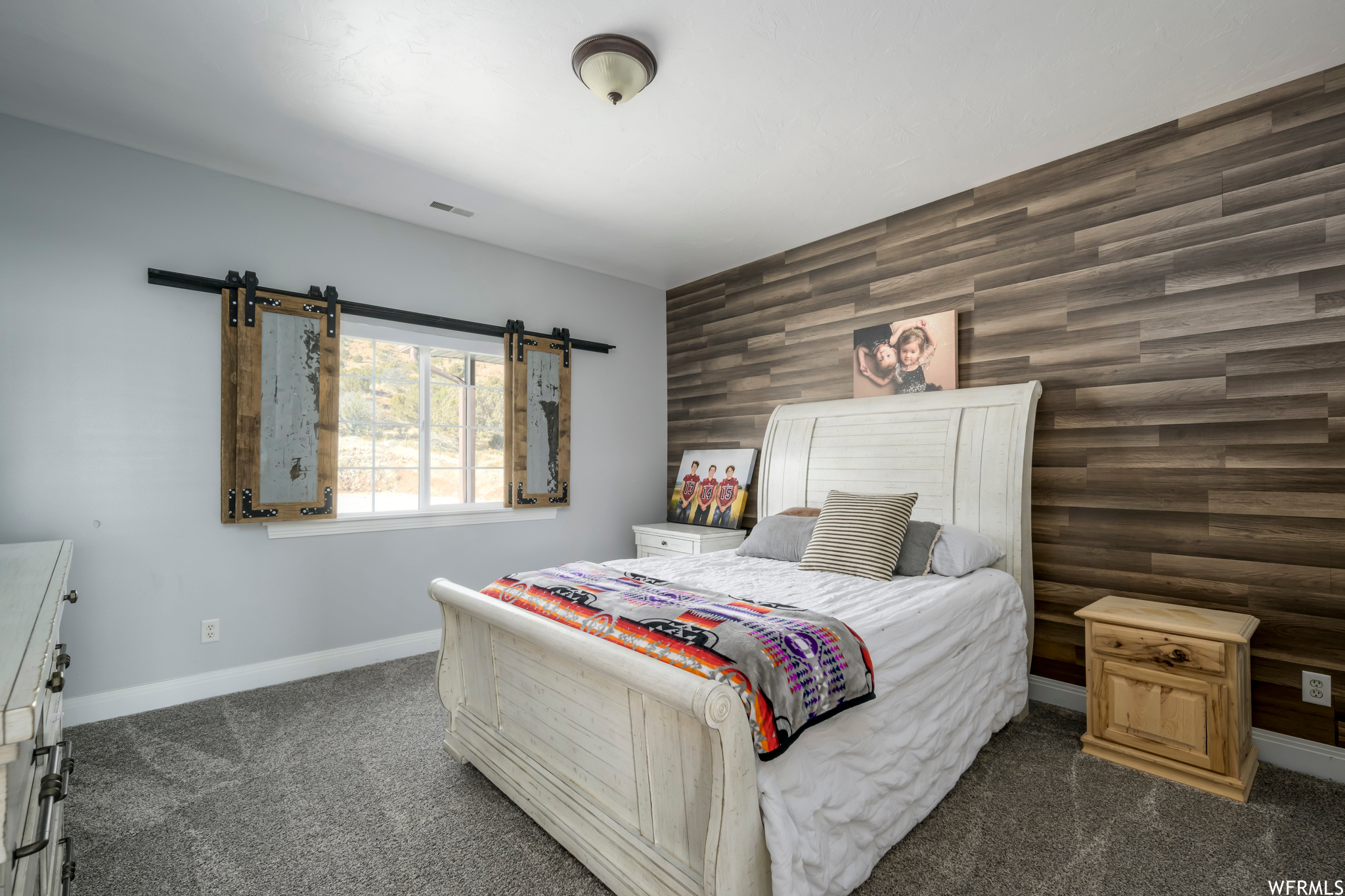 Carpeted bedroom featuring a barn door and wood walls