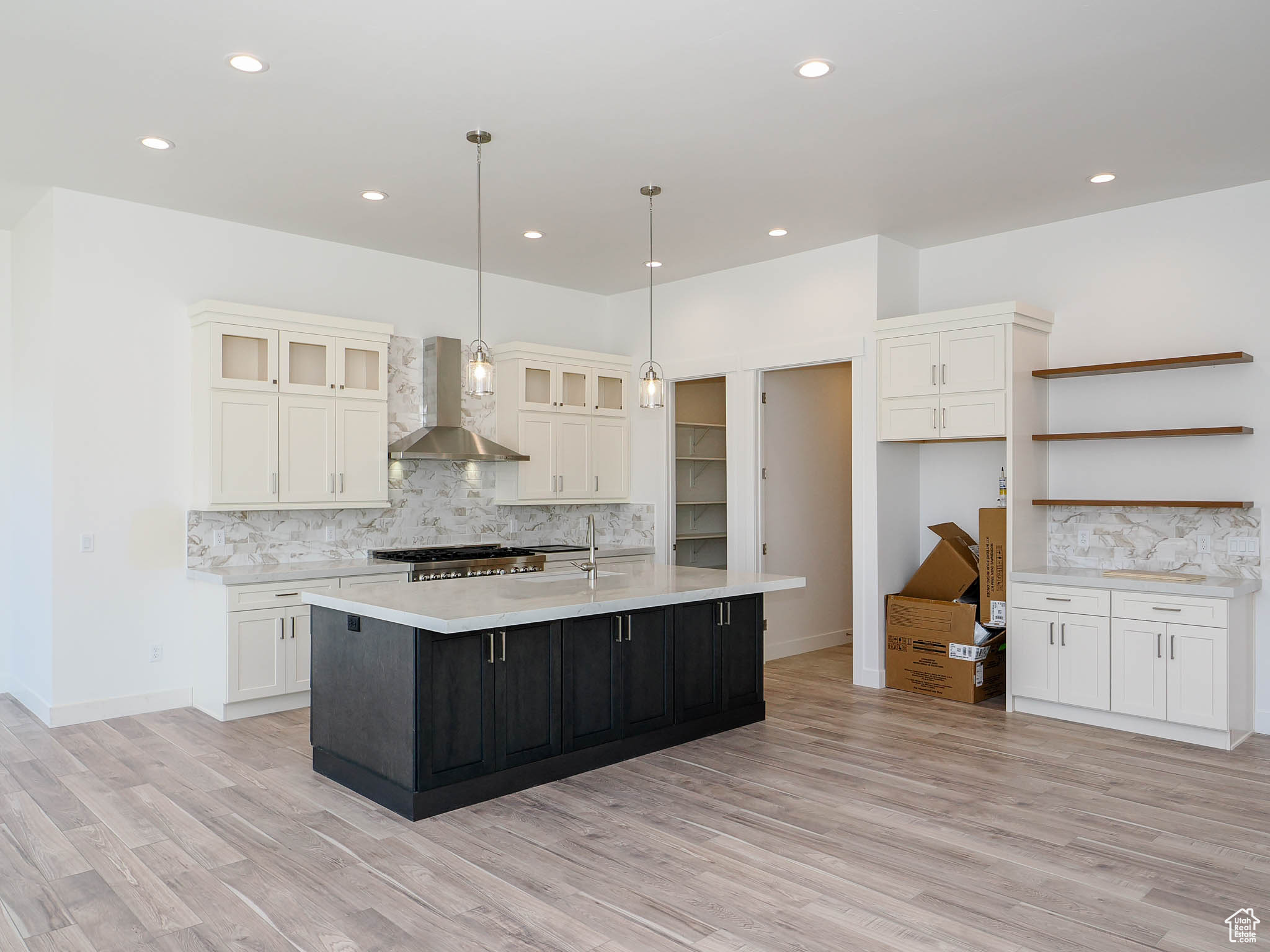 Kitchen with wall chimney exhaust hood, light hardwood / wood-style flooring, a kitchen island with sink, and white cabinets