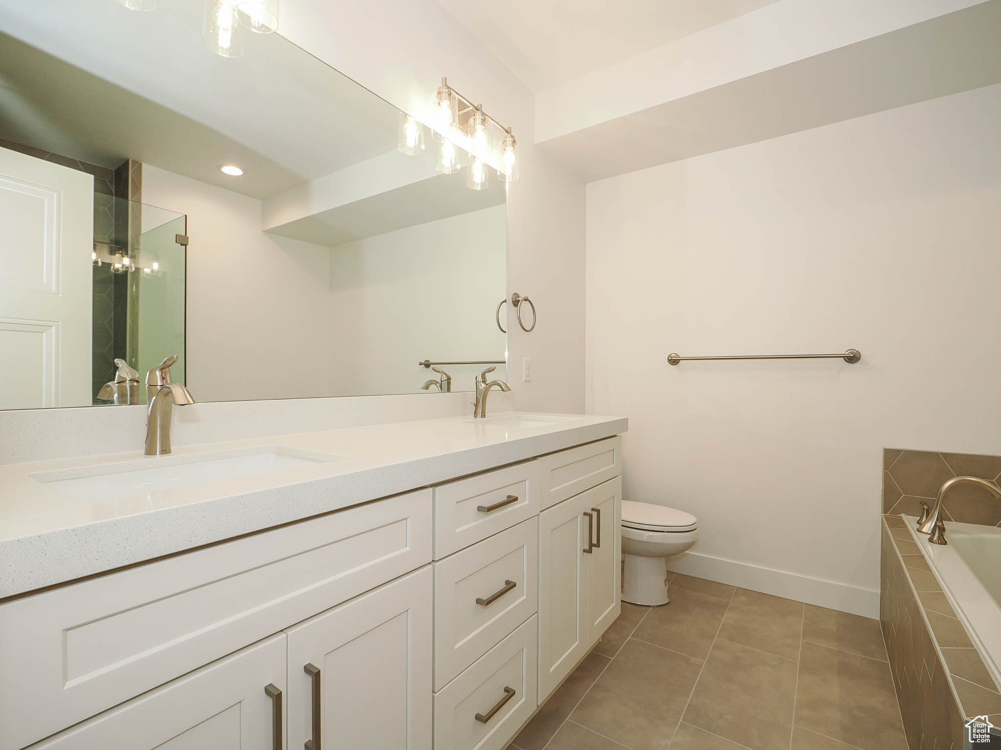 Bathroom featuring toilet, tiled tub, double sink vanity, and tile floors