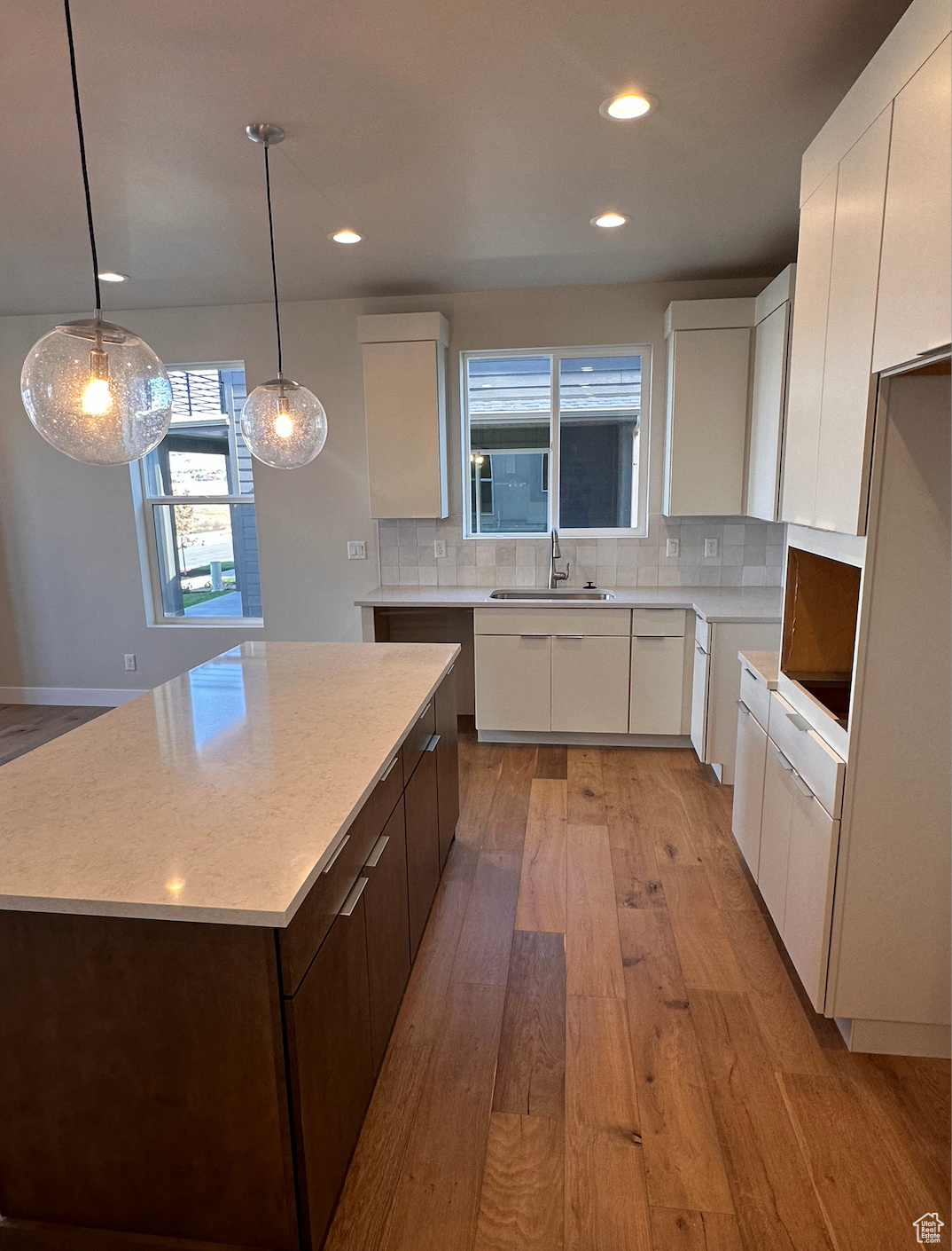 Kitchen with light wood-type flooring, white cabinetry, hanging light fixtures, a kitchen island, and backsplash